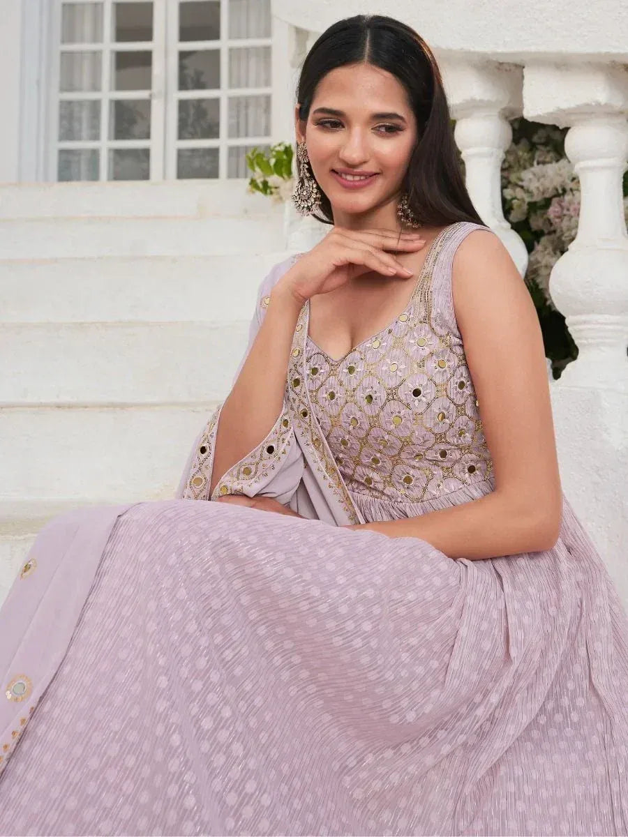 Woman in pastel pink embroidered ethnic gown with mirror work, sitting on white steps