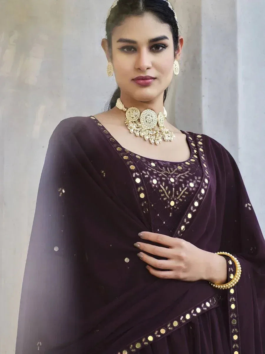 Woman in dark purple embroidered Indian salwar kameez with gold jewelry, dupatta draped