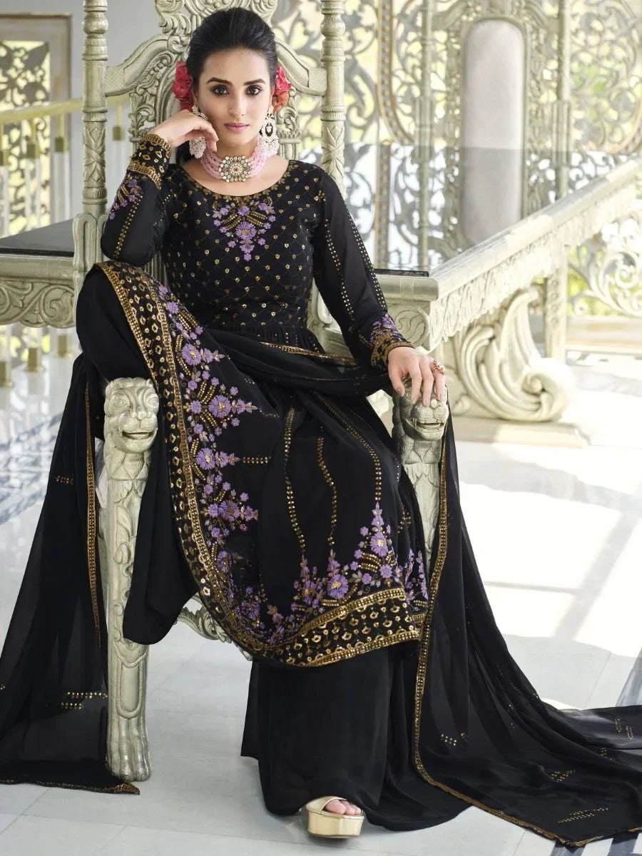 Woman in black and gold embroidered salwar kameez with purple floral accents, sitting on ornate chair