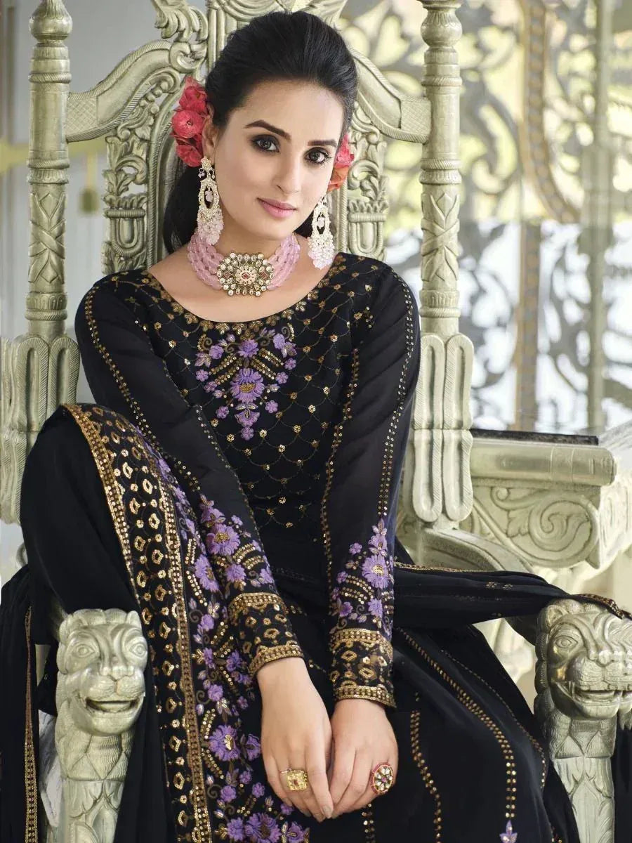 Black and purple embroidered salwar kameez with gold detailing, worn with statement jewelry and floral hair accessories.