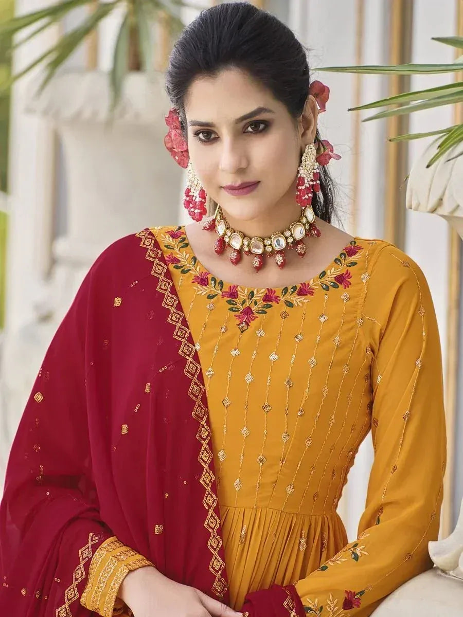 Woman in mustard yellow embroidered ethnic gown with maroon dupatta and statement jewelry