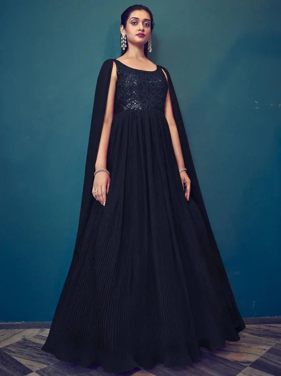 Woman wearing black sequin embroidered ethnic gown with cape sleeves, standing indoors