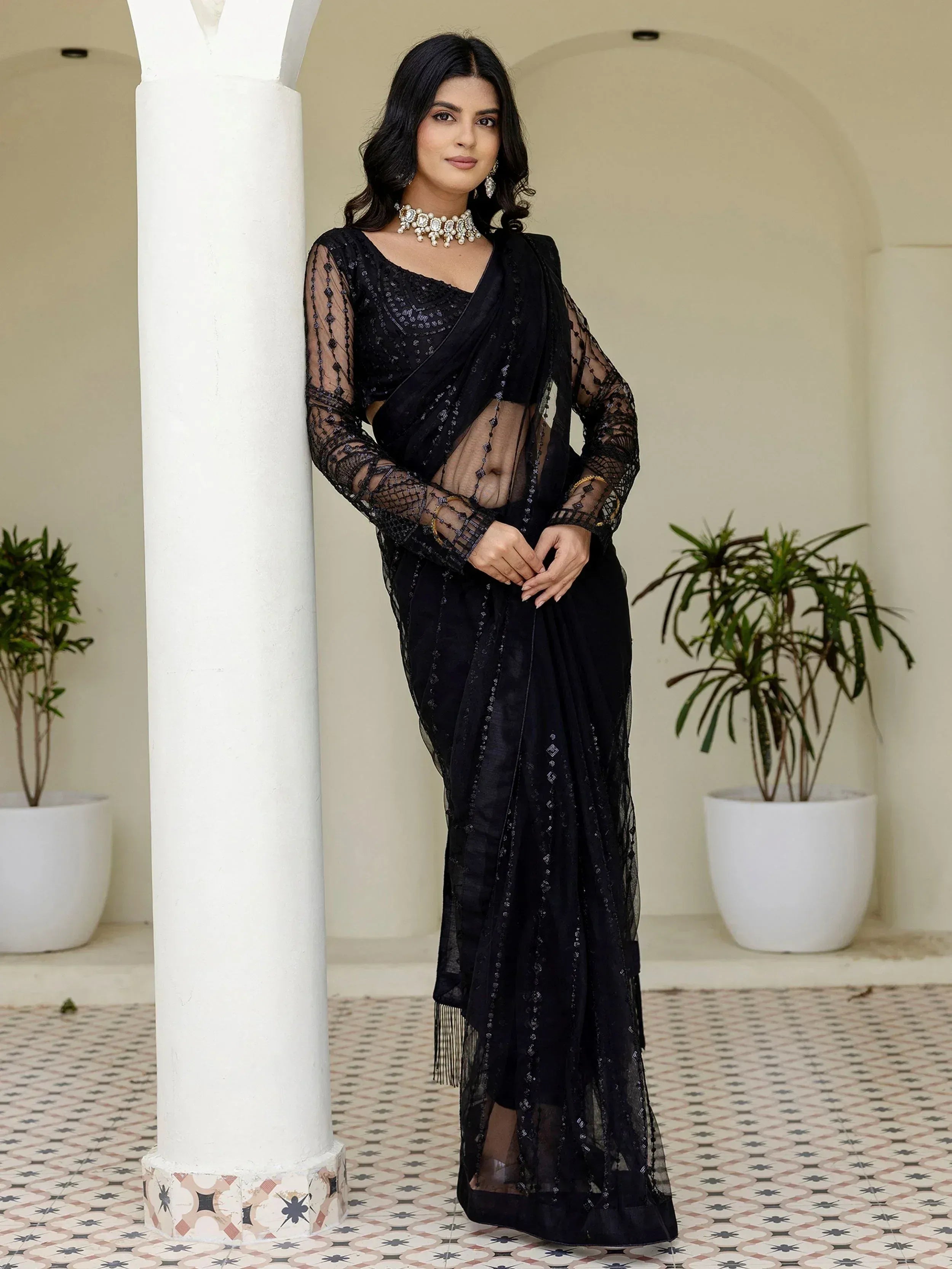 Black embroidered saree with sheer sleeves and statement jewelry, styled for Indian ethnic wear