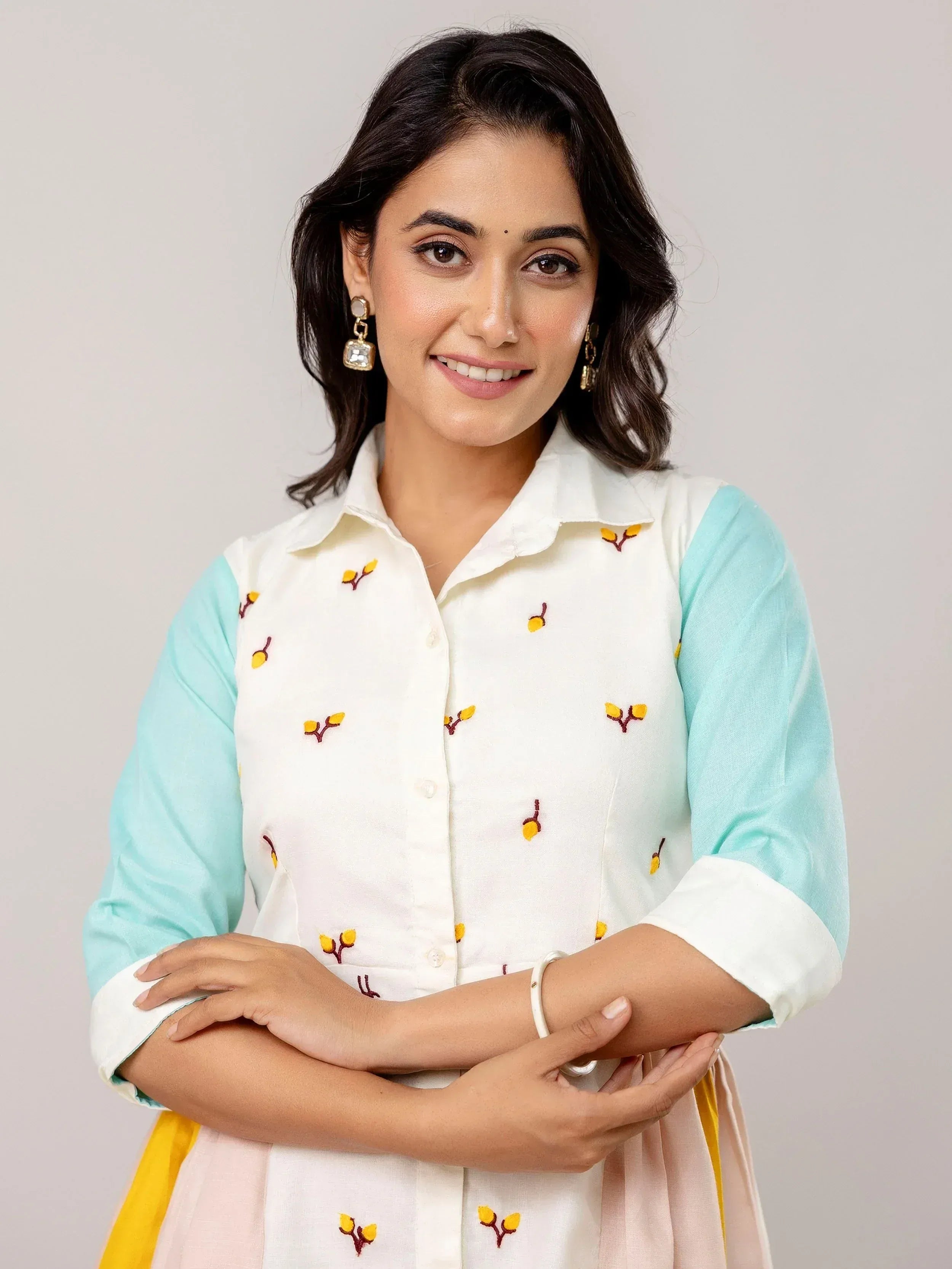 Woman in white and mint ethnic kurta with yellow floral embroidery, paired with pastel skirt and statement earrings