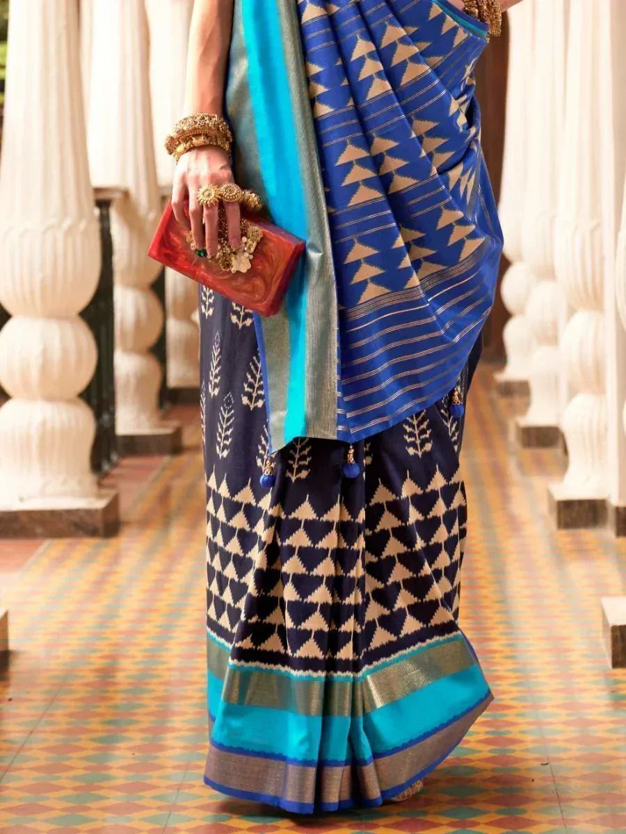 Blue and navy geometric print saree with gold motifs, paired with turquoise border and clutch, perfect for ethnic occasions.