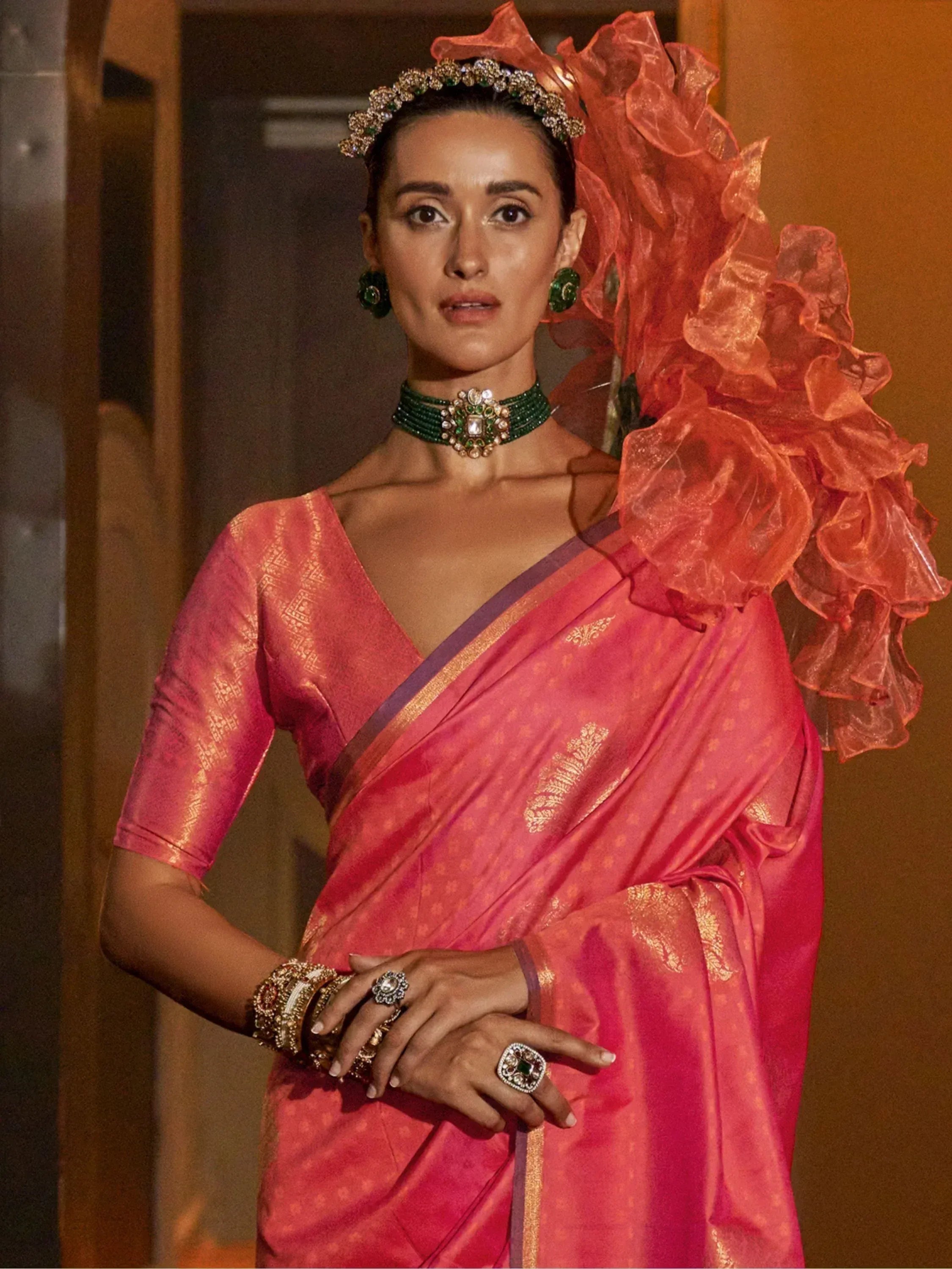 Woman in pink designer saree with gold patterns, emerald jewelry, and ruffled dupatta for ethnic occasions