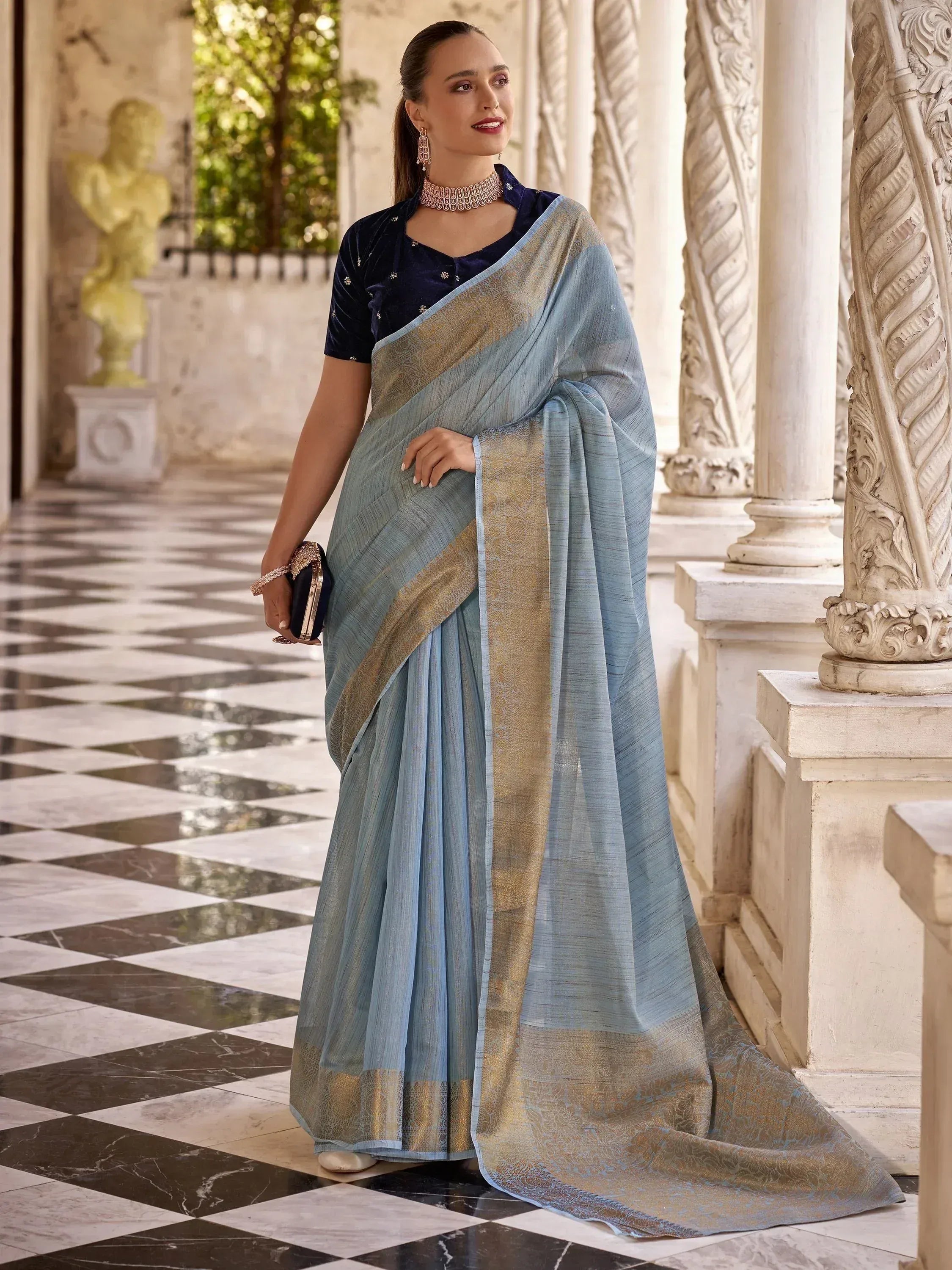 Elegant light blue saree with gold border, paired with navy velvet blouse, perfect for Indian ethnic occasions.
