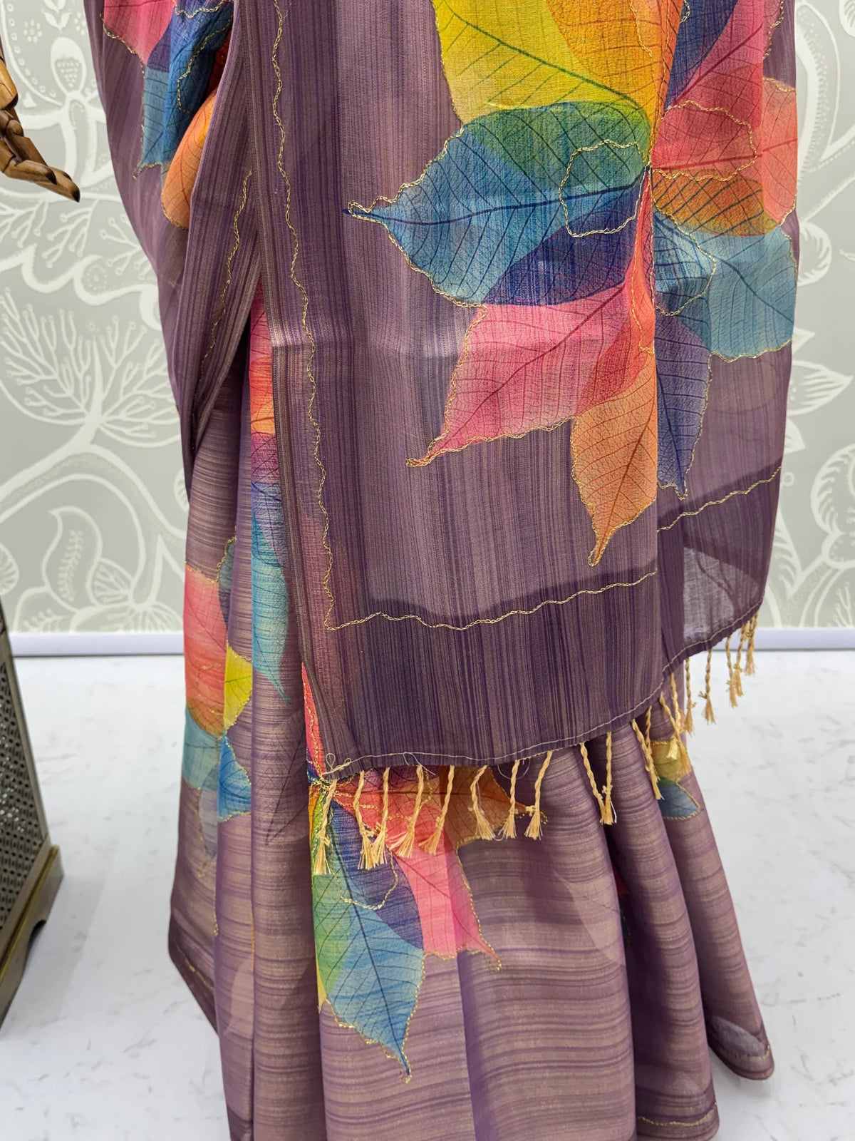 Purple designer saree with colorful rainbow leaf prints and gold tassel detailing.