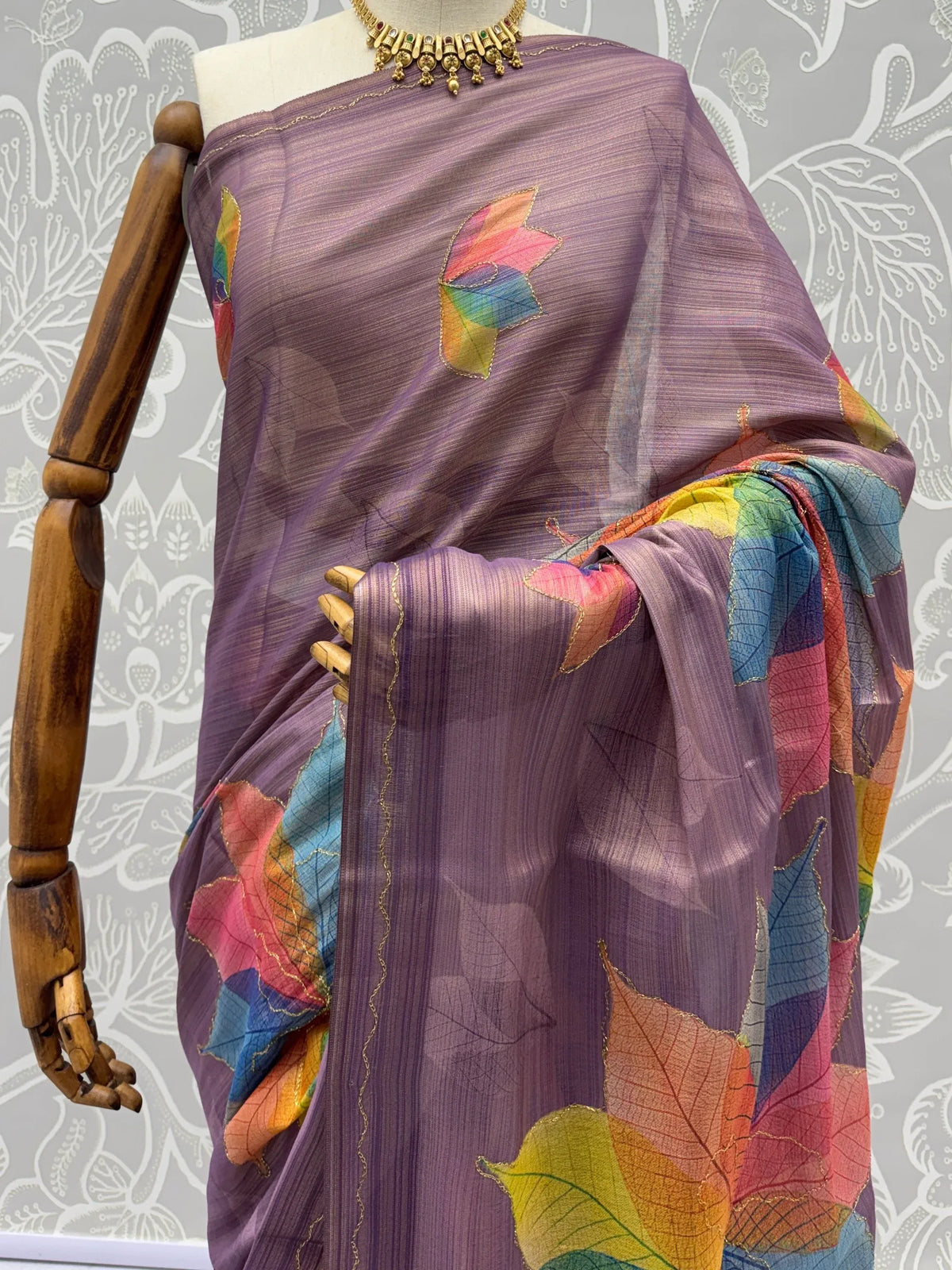 Purple sheer designer saree with colorful leaf embroidery on a mannequin