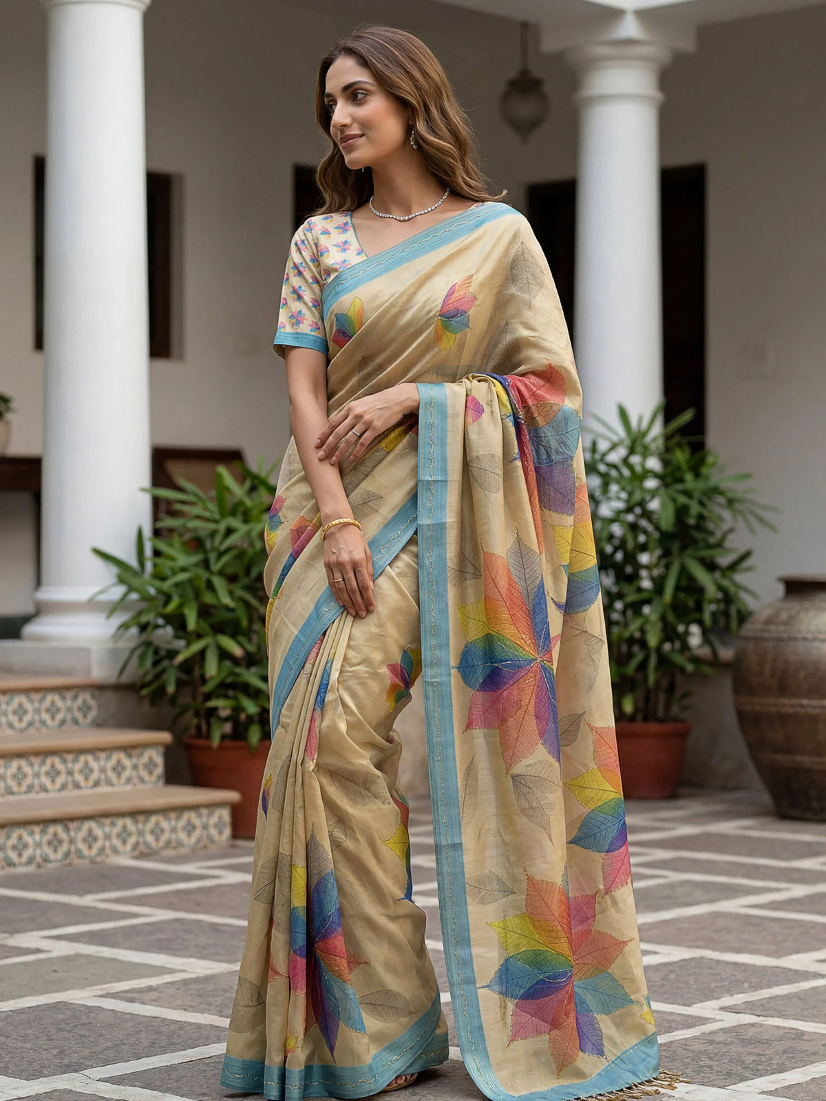 Woman wearing a beige designer saree with colorful leaf prints and light blue border
