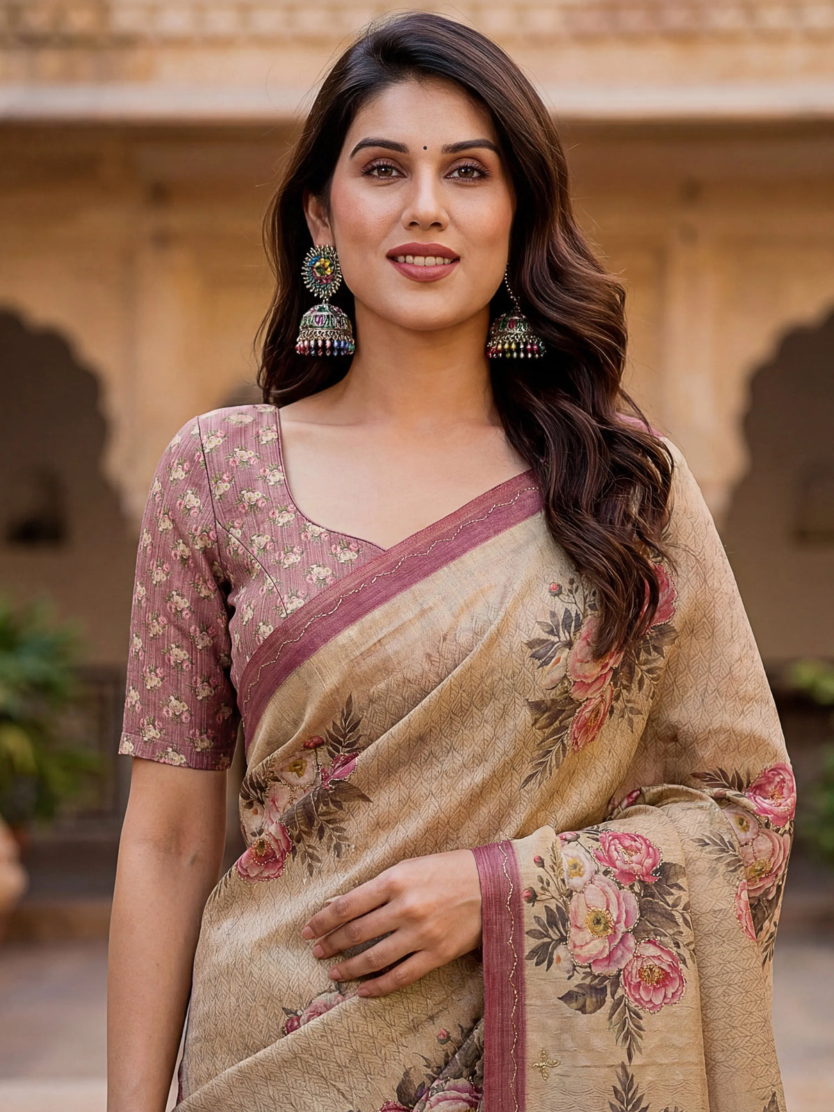 Woman wearing a beige floral printed saree with a mauve patterned blouse and statement jhumkas