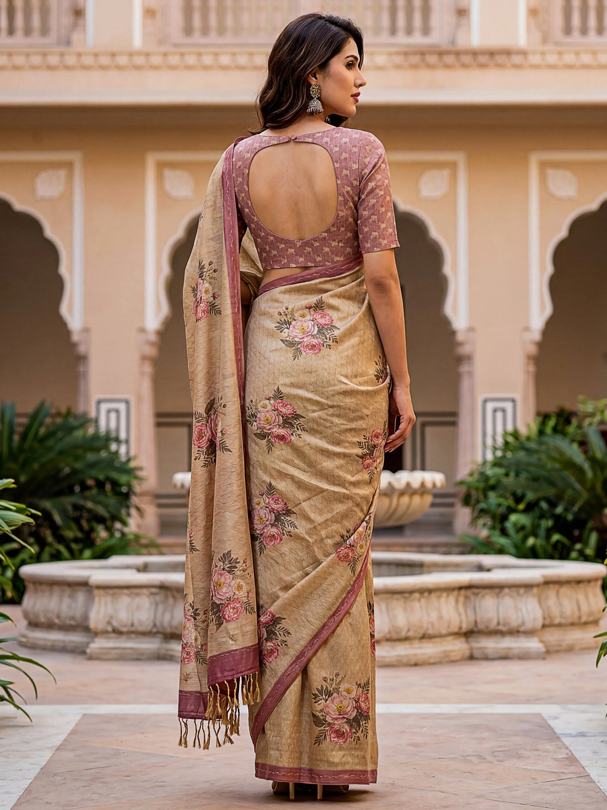Woman in a beige floral print saree with a backless mauve blouse standing in a courtyard