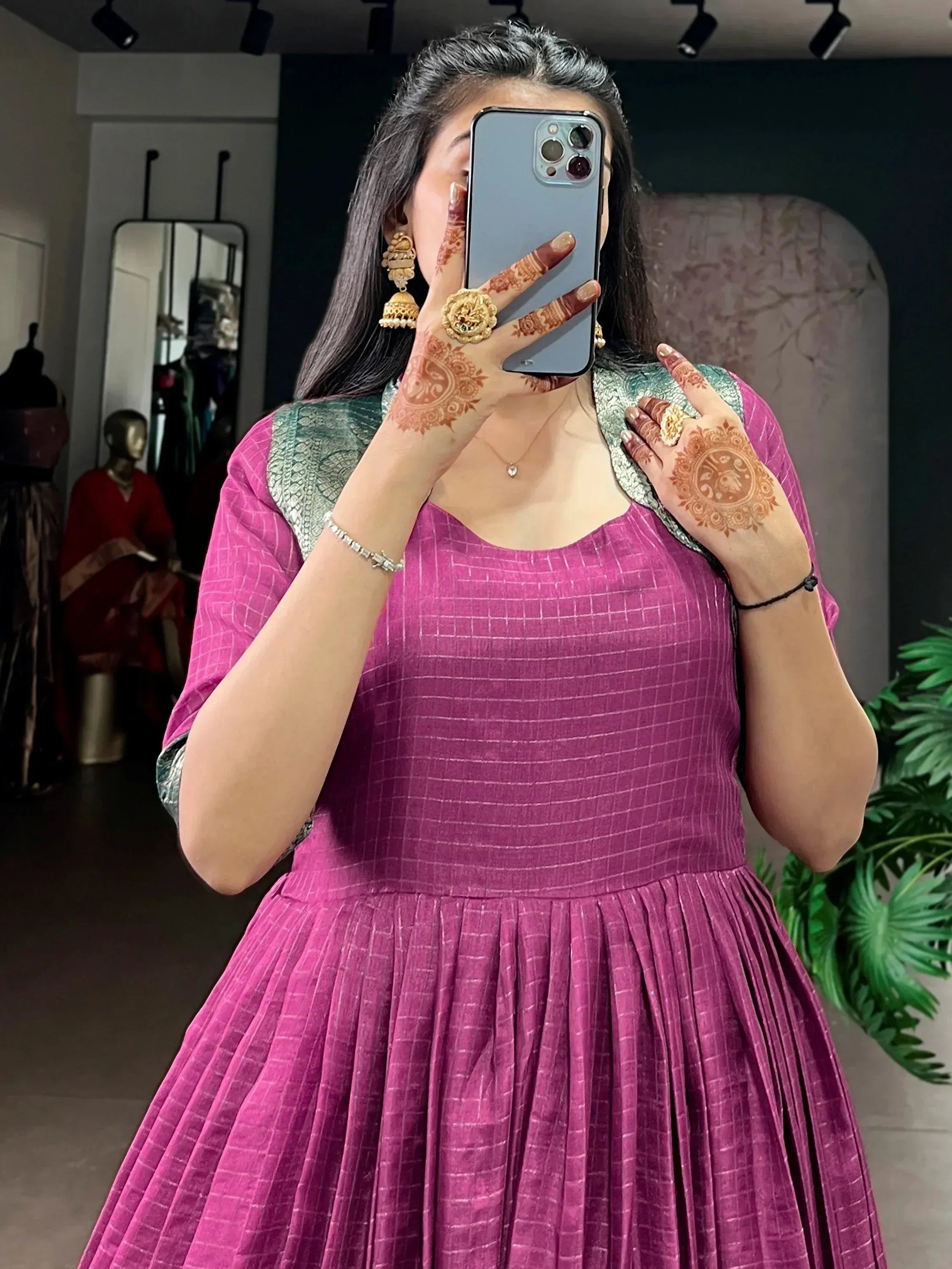 Woman in pink ethnic gown with henna hands, gold jewelry, mirror selfie at boutique