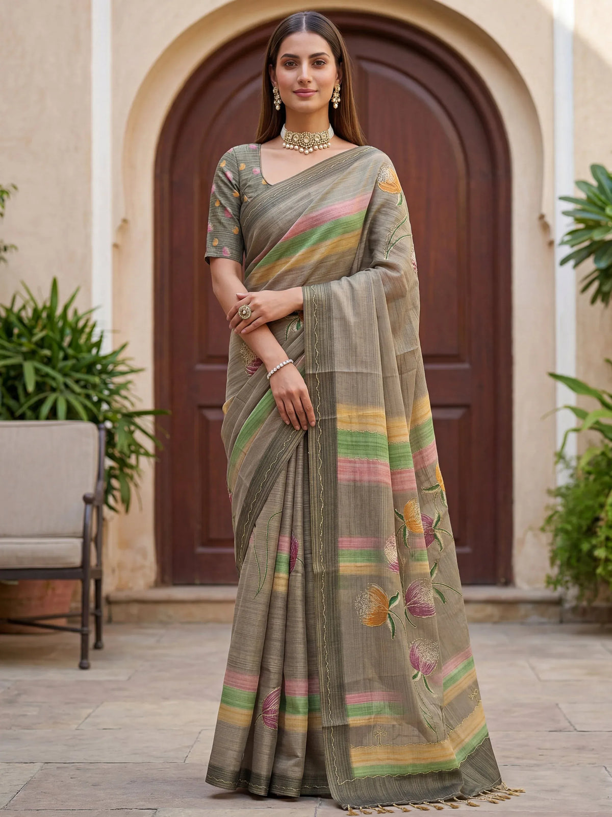 Woman wearing a grey linen saree with colorful stripes and floral embroidery.