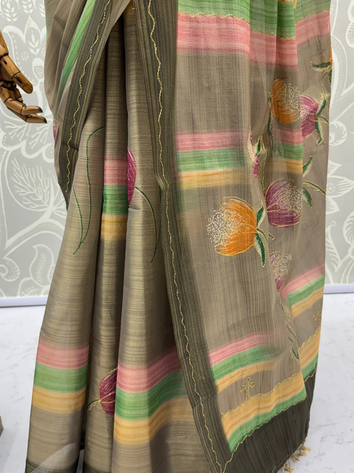 Close-up of a grey designer saree with colorful stripes and floral embroidery.