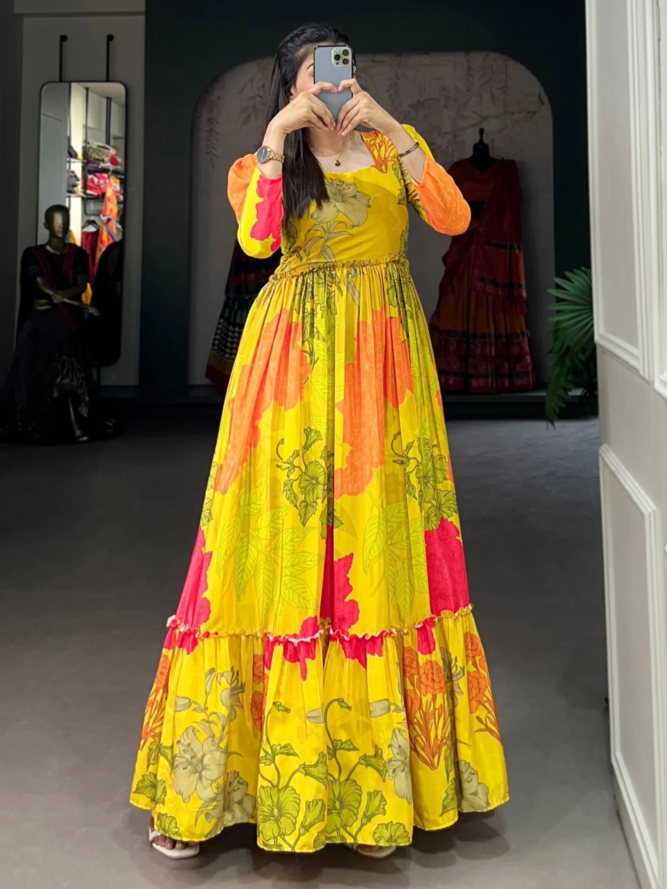 Woman in a yellow floral long ethnic gown taking a mirror selfie indoors