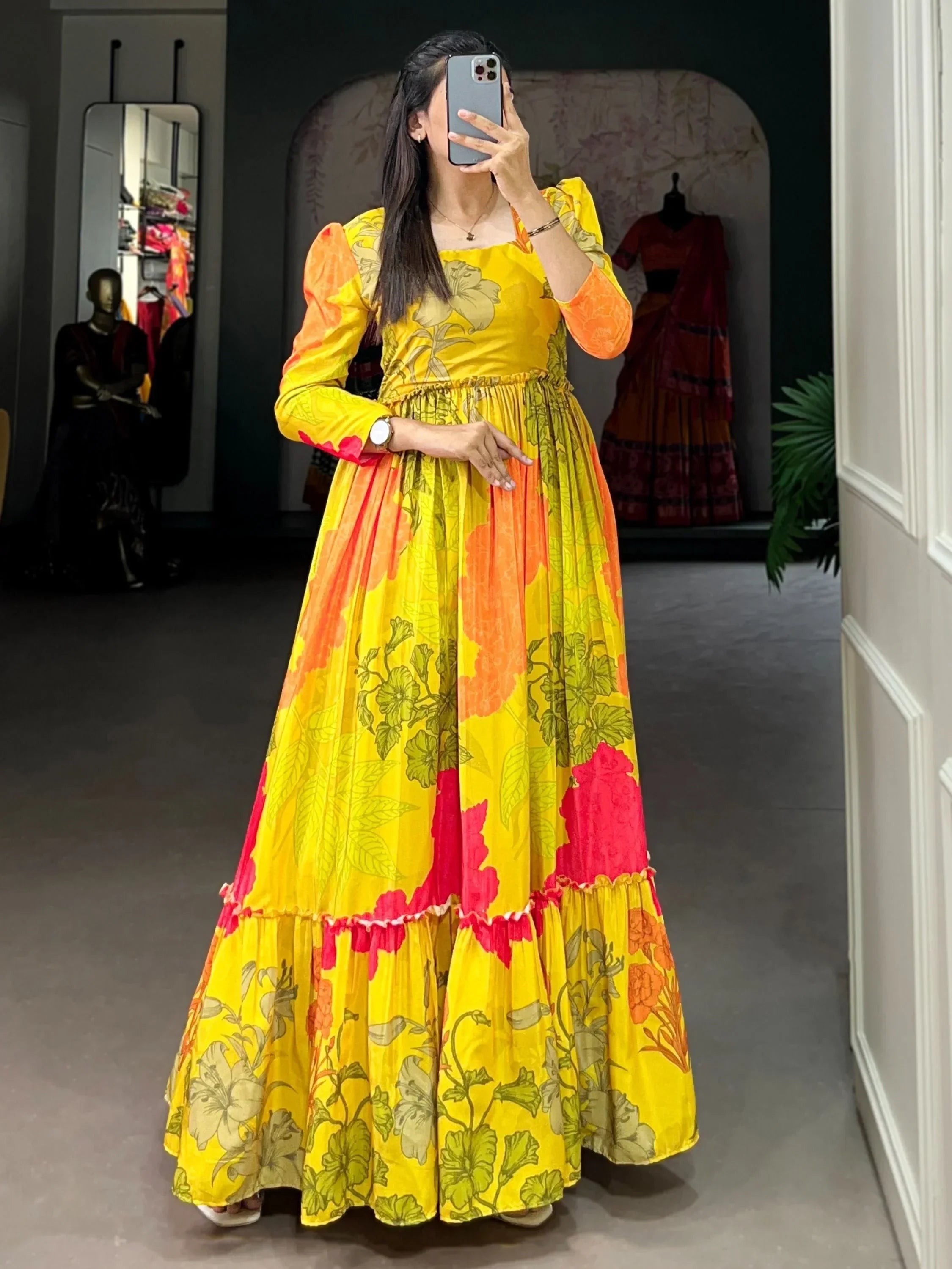Woman wearing yellow floral printed ethnic gown with long sleeves, taking a mirror selfie.