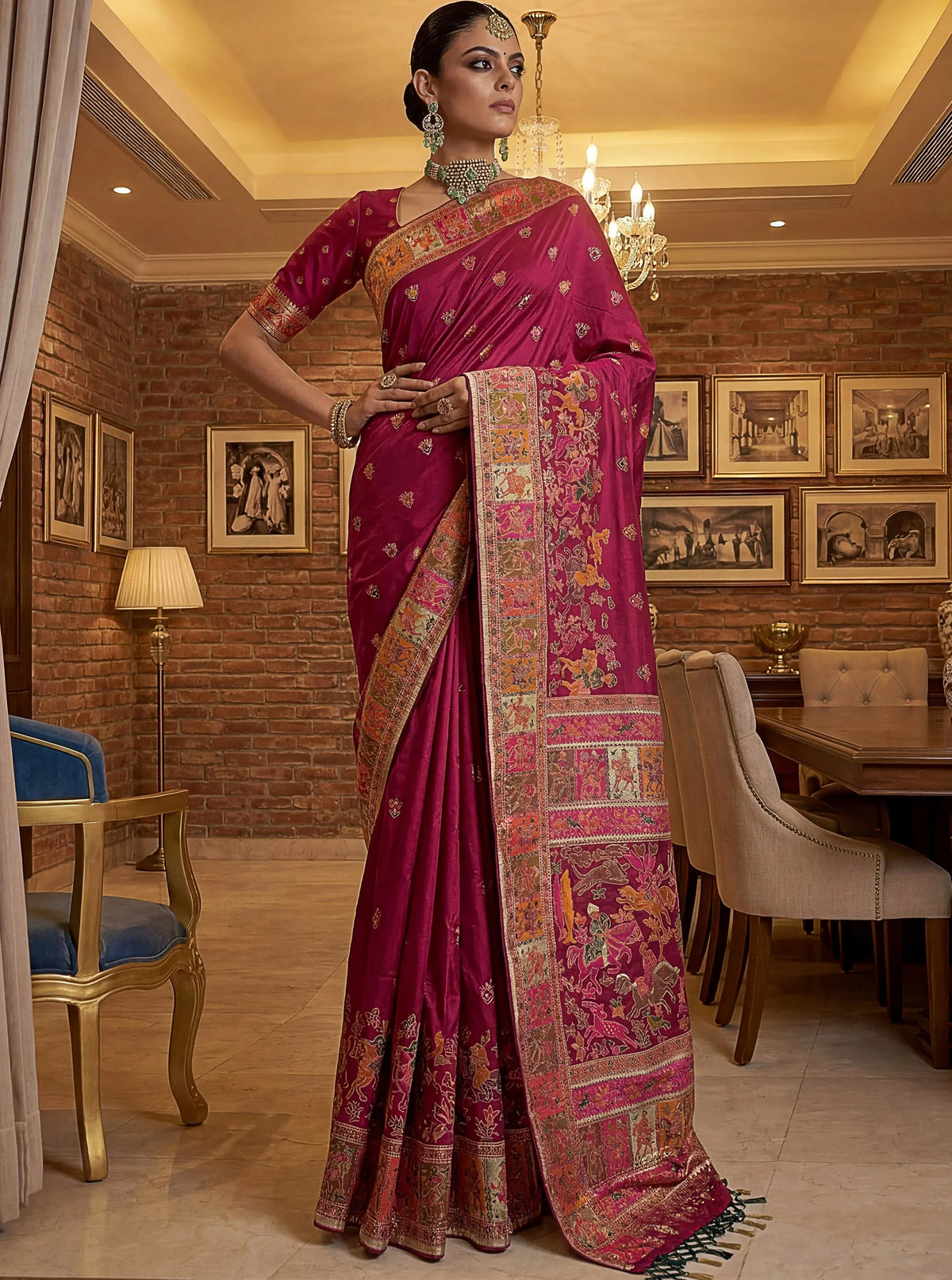 Woman wearing a magenta designer silk saree with intricate gold zari borders and embroidery