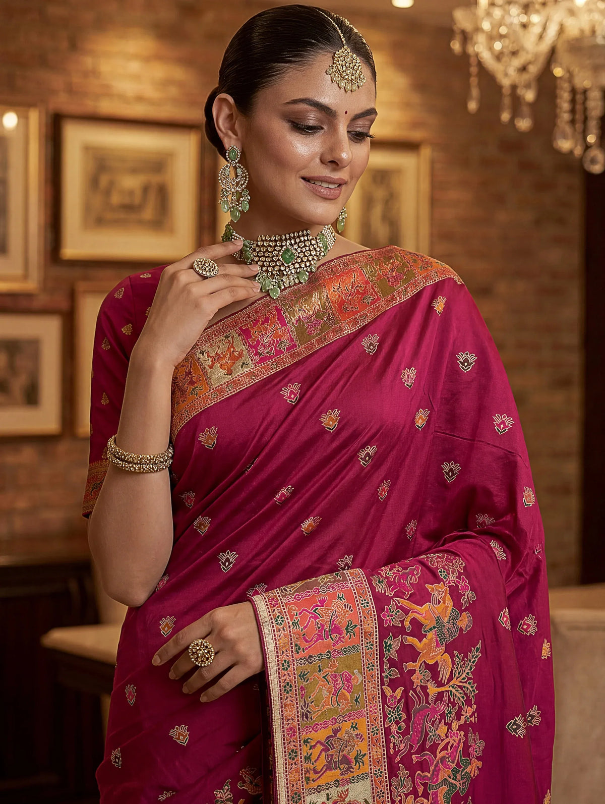 Woman wearing a magenta silk saree with gold zari borders and traditional emerald jewelry