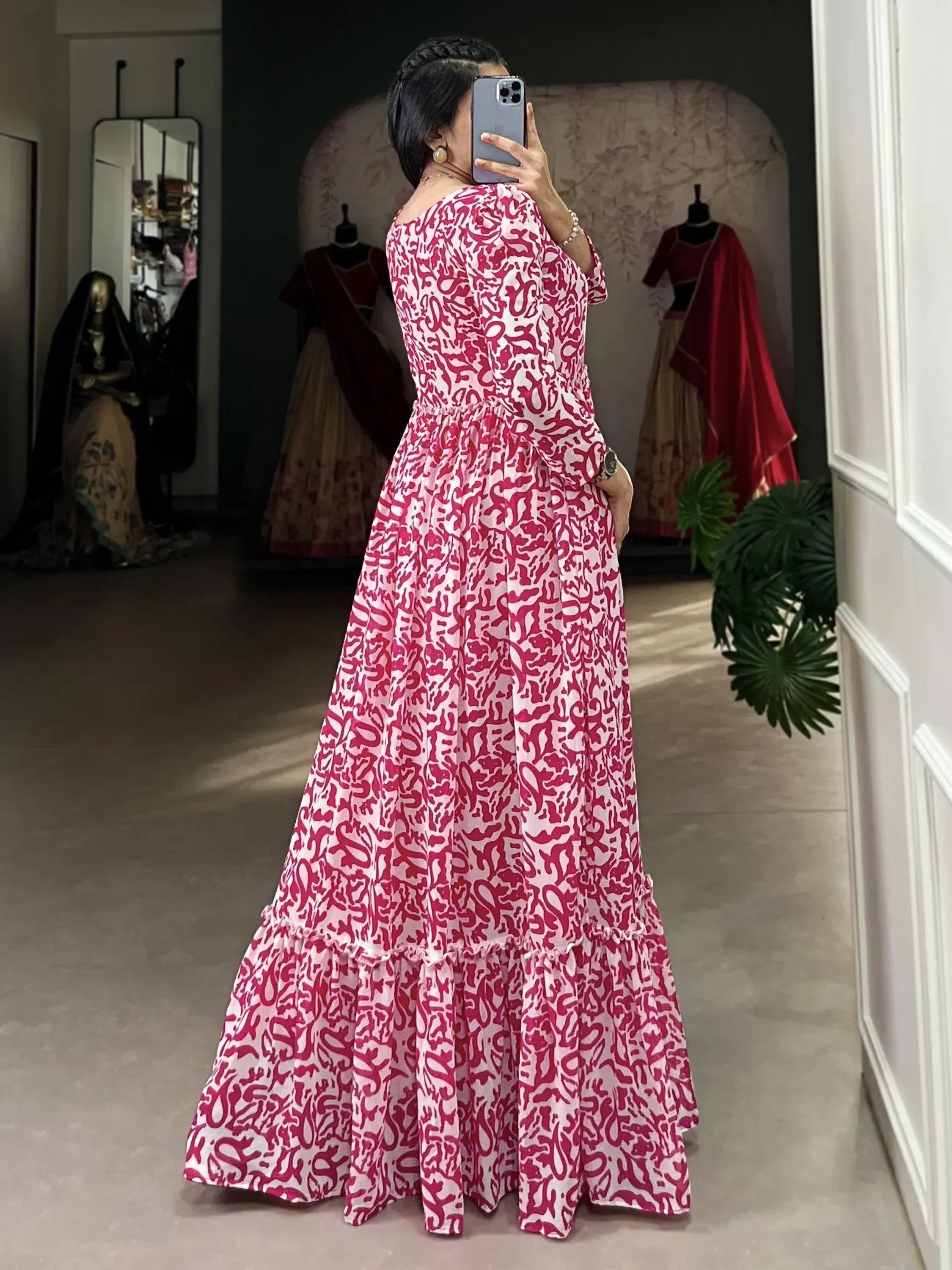 Woman in pink and white printed ethnic gown, mirror selfie in boutique with mannequins