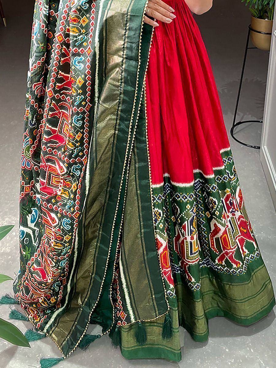 Red and green embroidered lehenga choli with intricate tribal print and tassels, perfect for ethnic occasions.