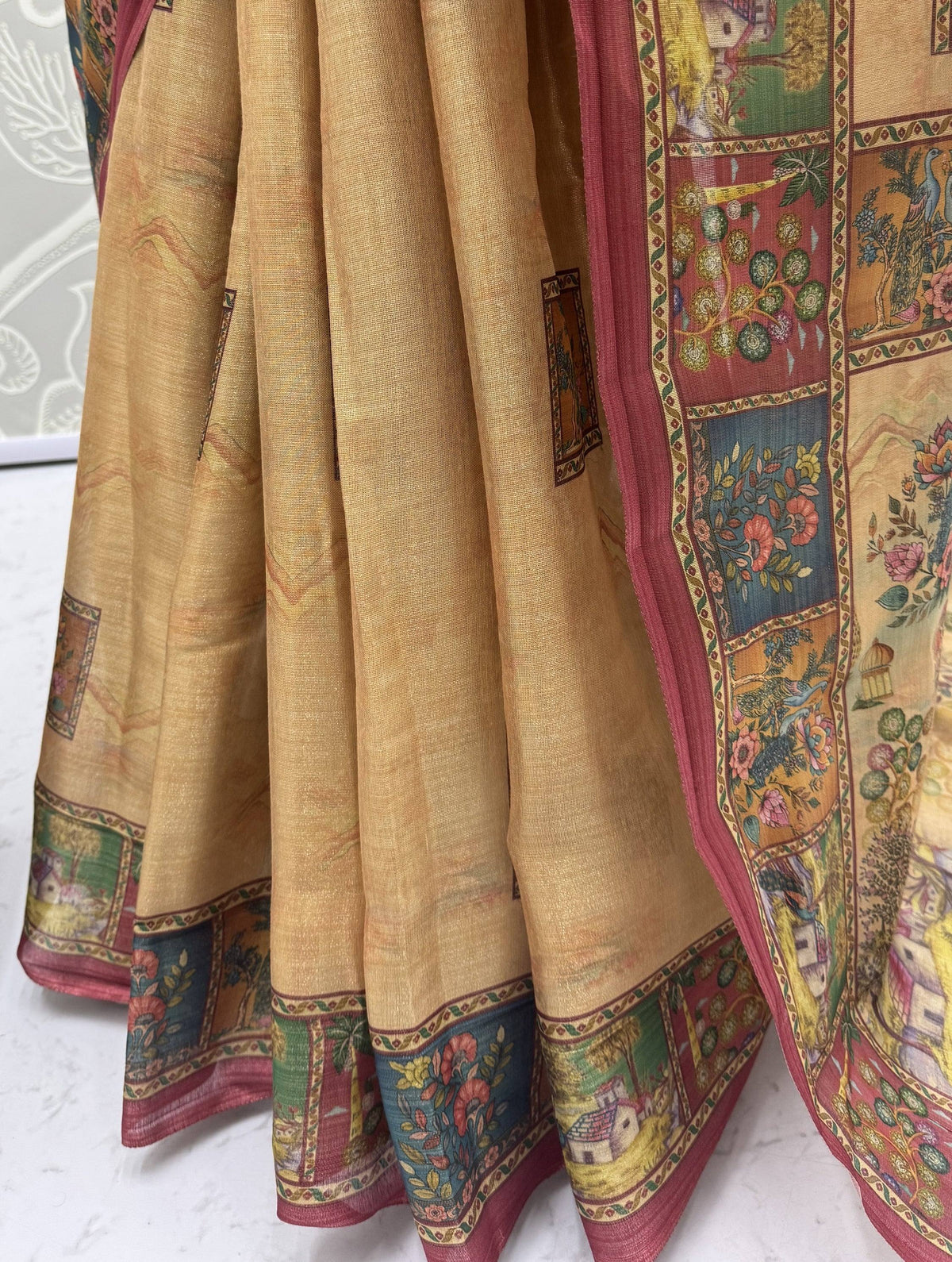 Close-up of a beige ethnic saree with floral and landscape prints and a pink border.