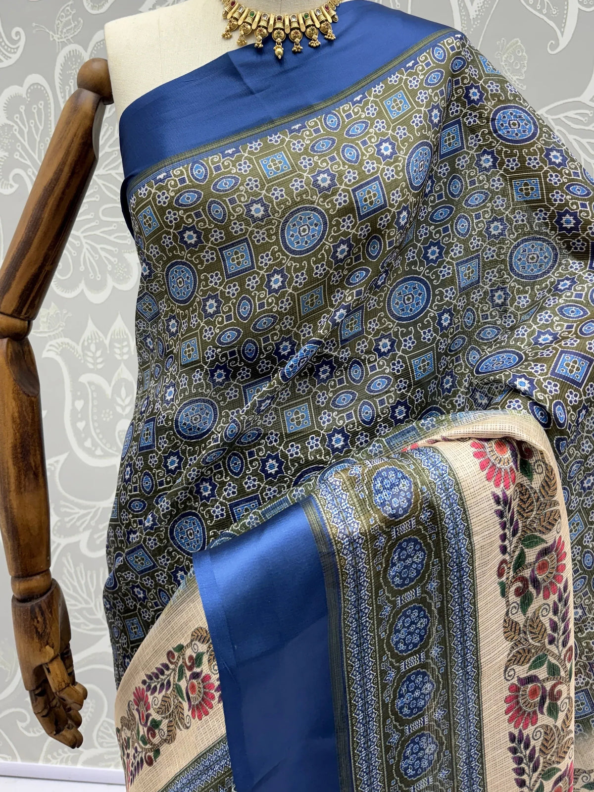 Olive green and blue printed silk saree with floral border on a mannequin