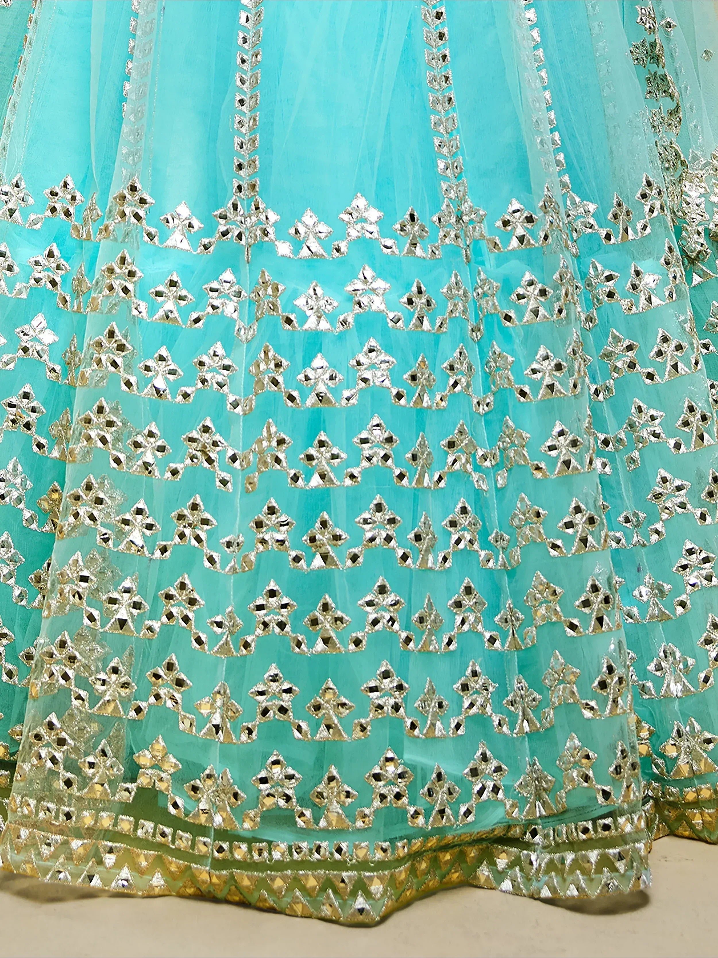 Turquoise lehenga with intricate silver mirror work and gold trim, perfect for Indian ethnic wear.