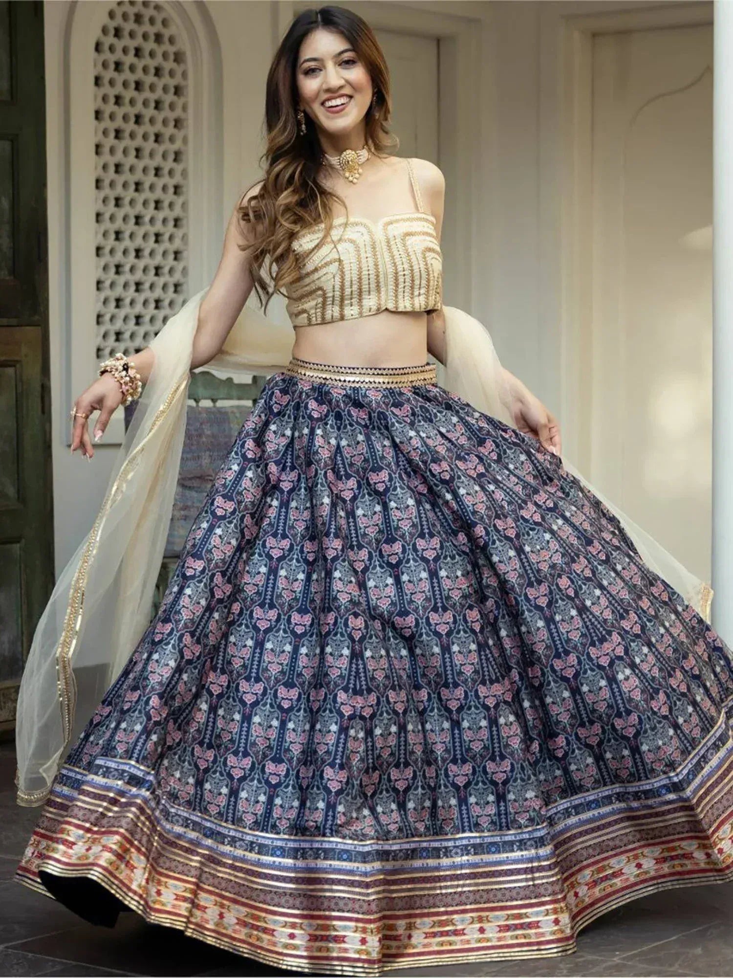 Woman in elegant Indian lehenga choli with floral print skirt and gold embellished crop top, perfect for festive occasions.