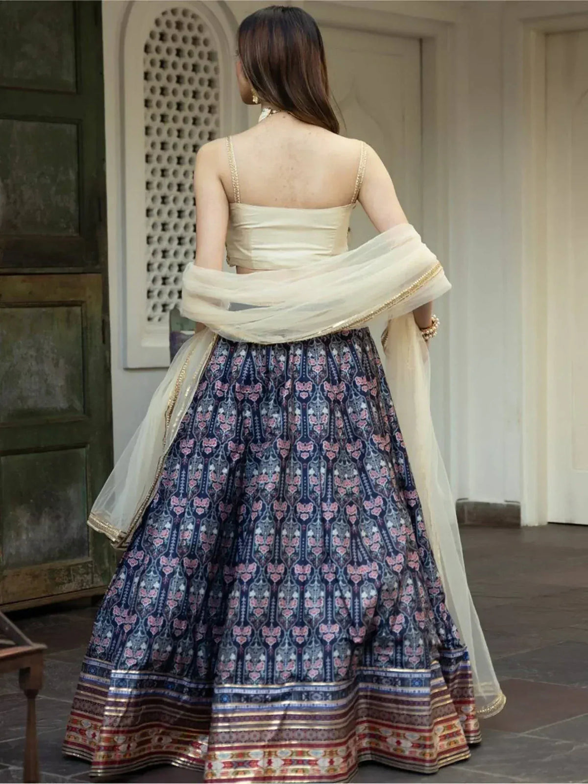 Back view of woman in navy floral lehenga choli with gold trim, cream dupatta, ethnic Indian wear