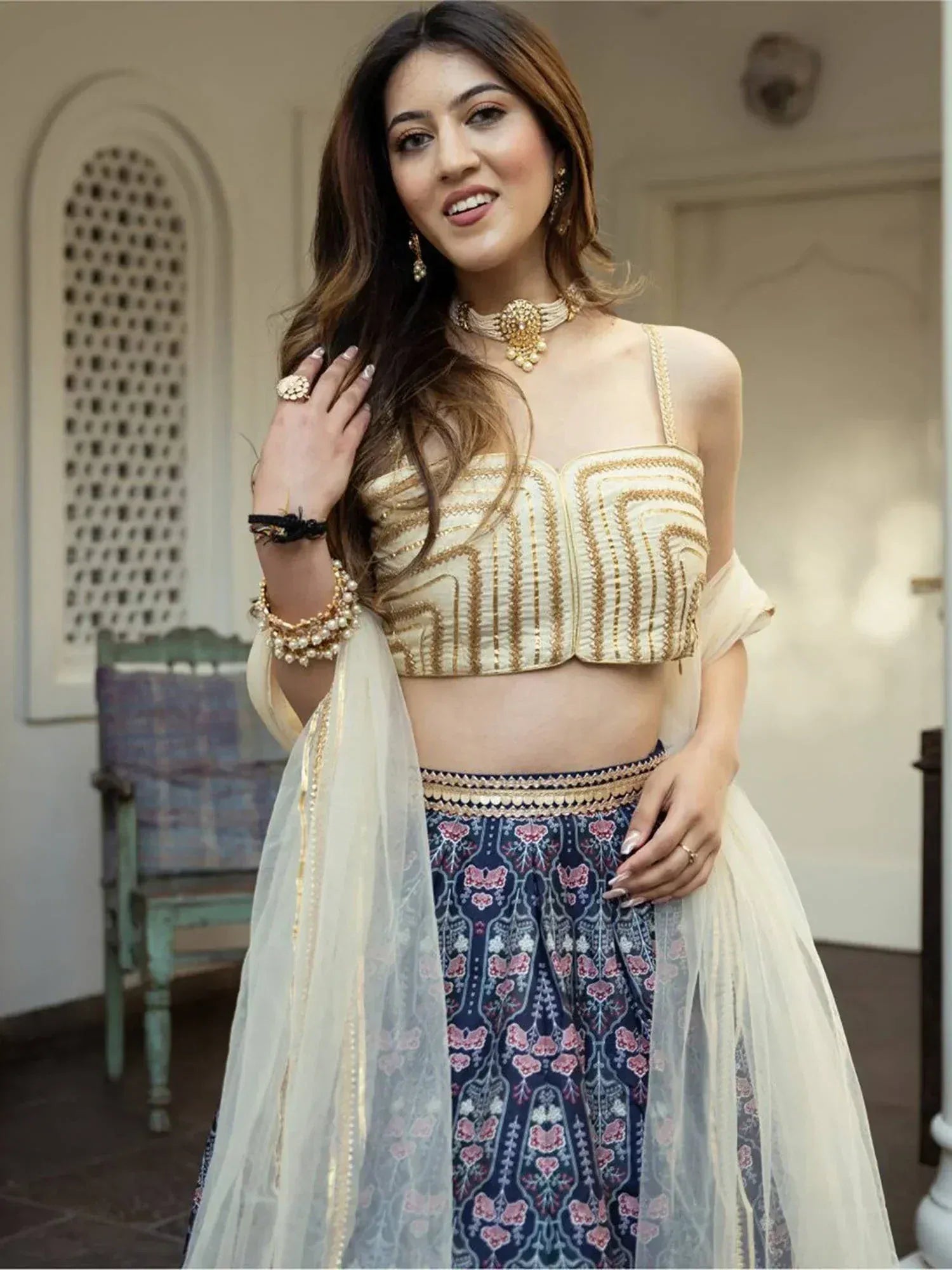 Elegant Indian ethnic wear: gold-embroidered crop top with floral skirt and sheer dupatta, perfect for festive occasions.