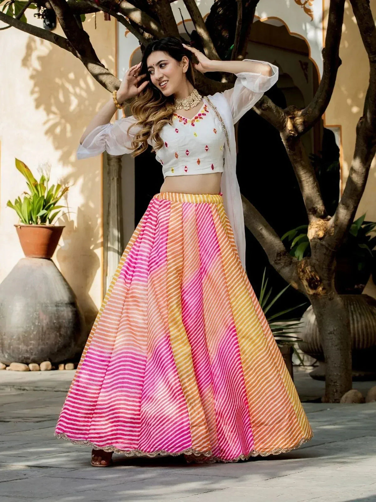 Woman in vibrant pink and orange striped lehenga with white embroidered blouse, styled for ethnic wear.