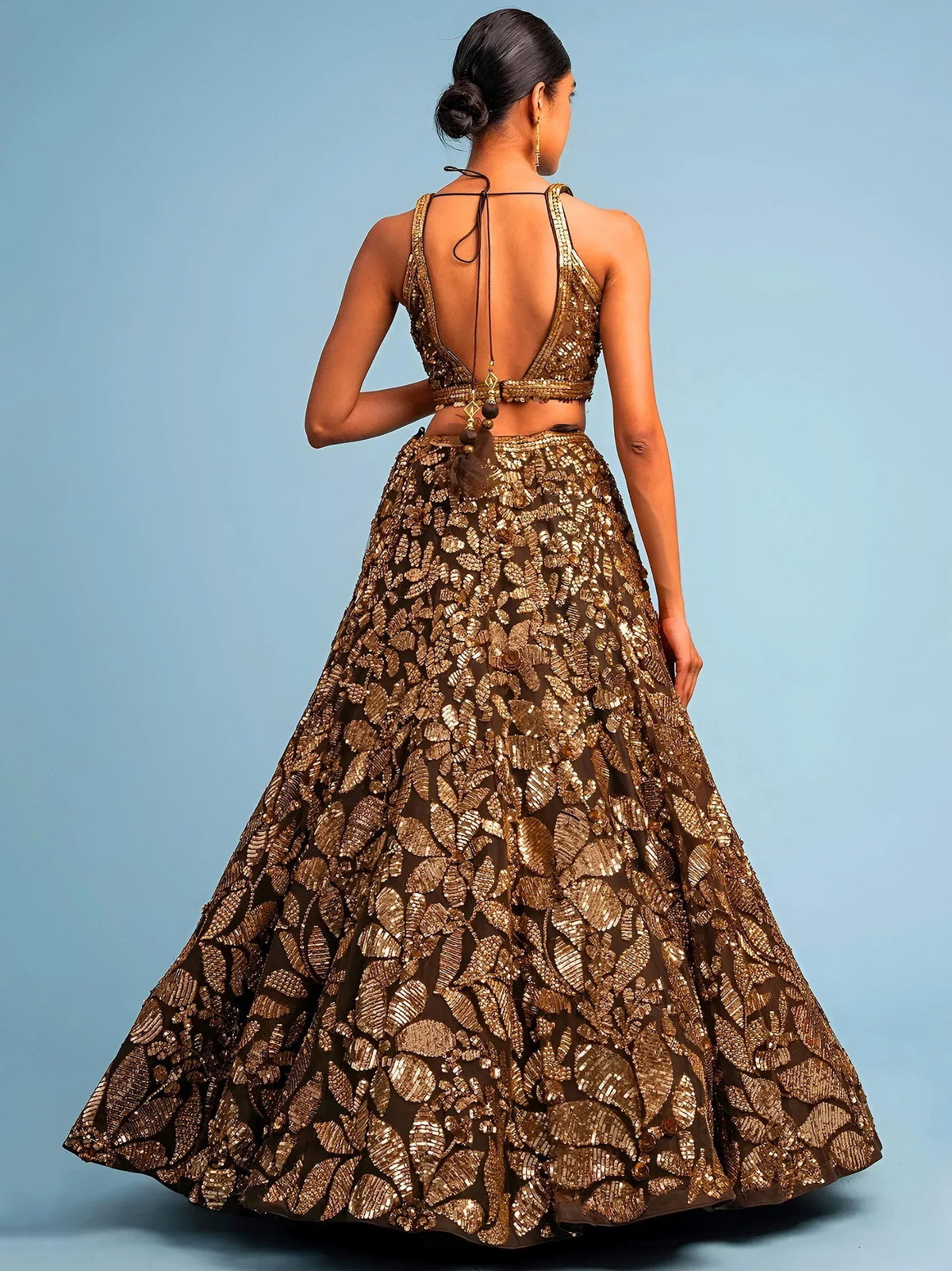 Back view of woman in gold-embellished designer lehenga choli with leaf pattern and open back, ideal for Indian ethnic wear.