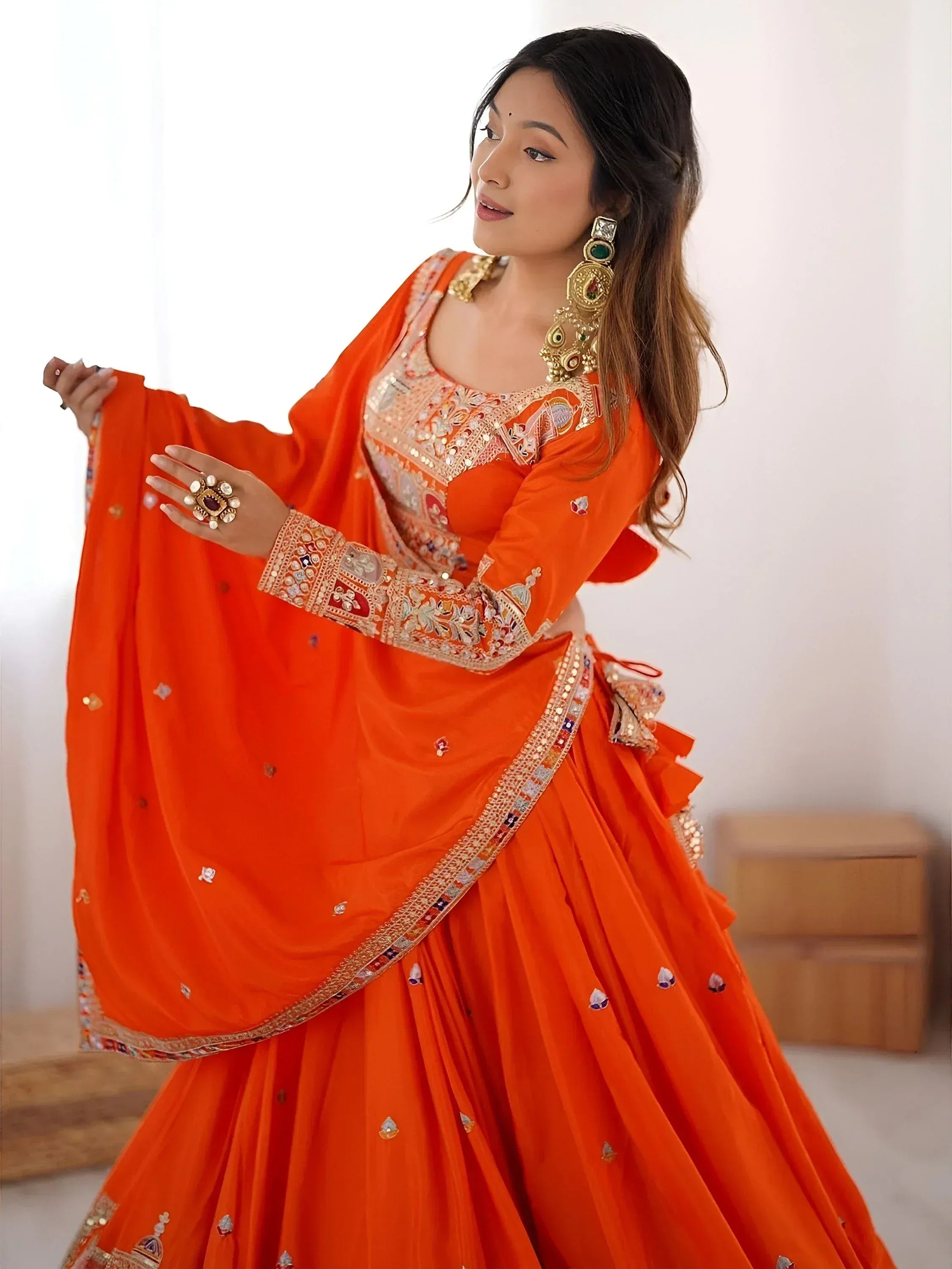 Vibrant orange designer lehenga choli with intricate embroidery and mirror work, perfect for Indian ethnic occasions.