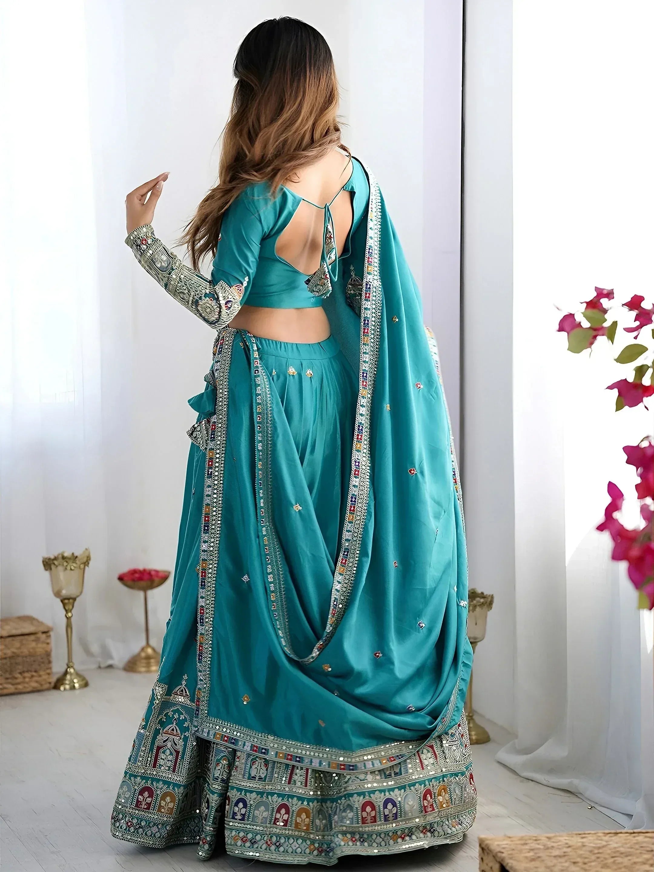 Teal designer lehenga choli with intricate mirror work and backless blouse, perfect for Indian ethnic wear occasions.