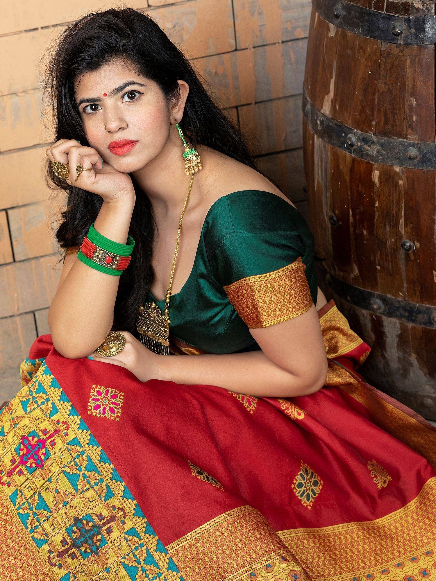 Woman in vibrant red and green Indian saree with gold embroidery, traditional jewelry, and off-shoulder blouse
