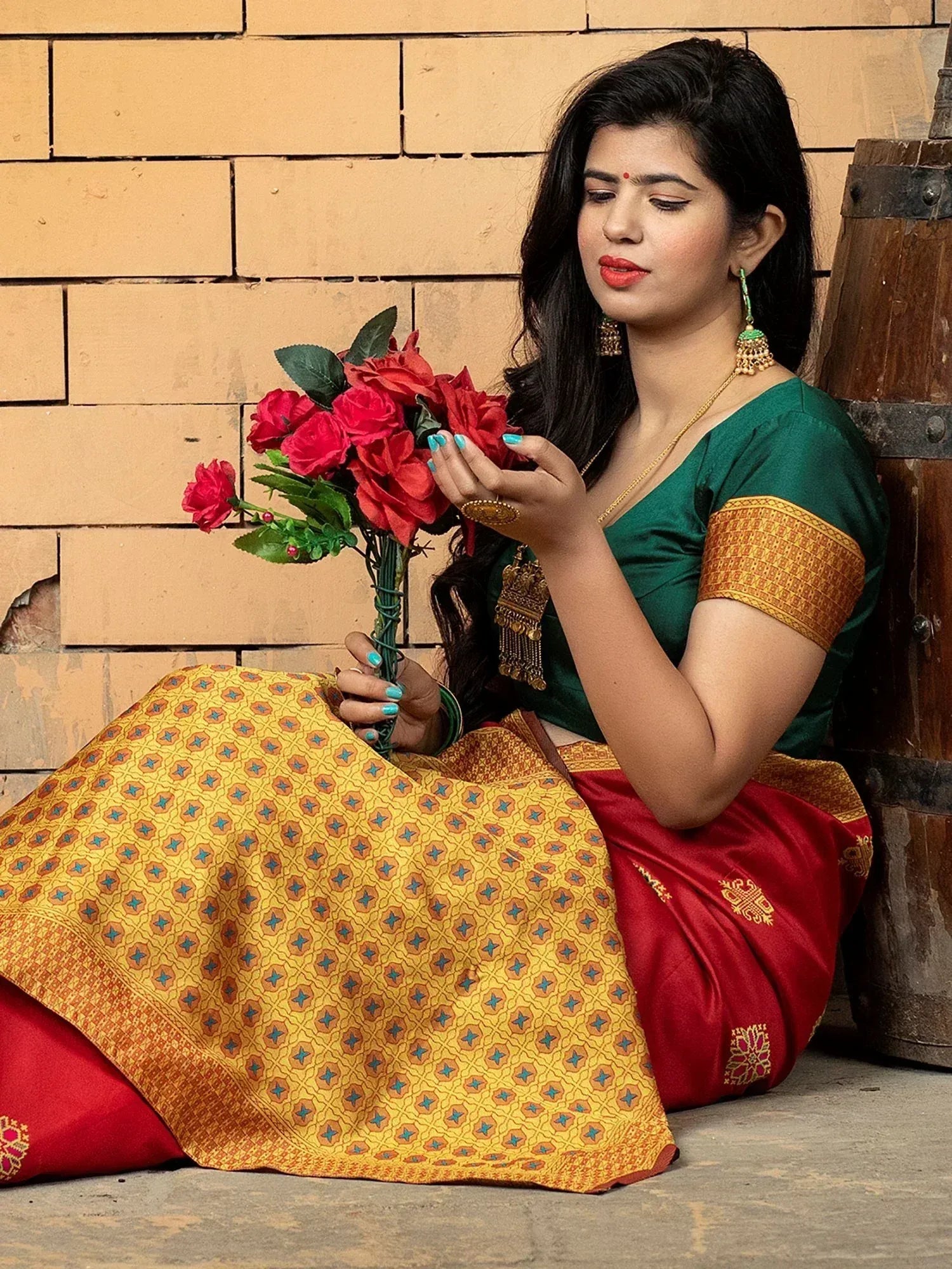 Woman in green blouse and red-yellow patterned saree holding red roses, traditional Indian ethnic wear