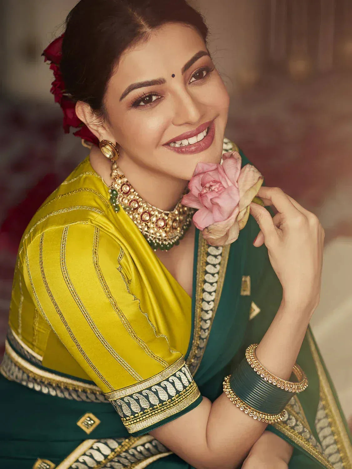 Woman in green and yellow designer saree with gold embroidery, traditional jewelry, and floral hair accessory