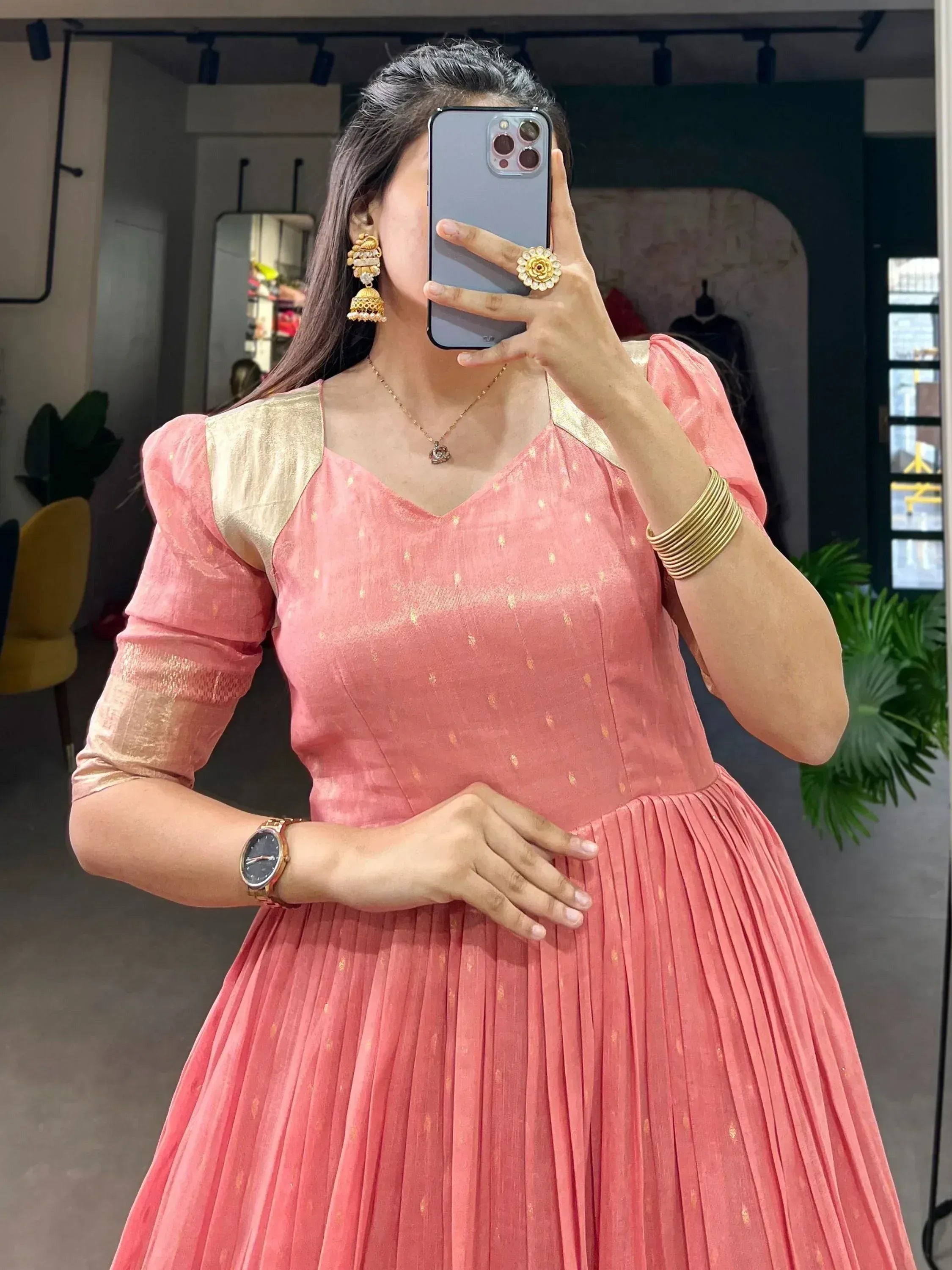 Pink ethnic gown with gold accents, puff sleeves, and pleated skirt, styled with jhumka earrings and bangles