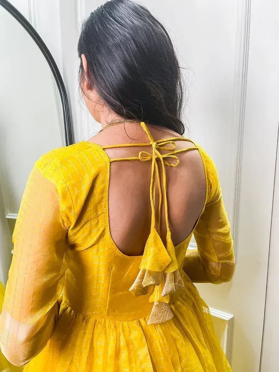 Back view of a woman wearing a yellow ethnic gown with tie-up tassels and sheer sleeves