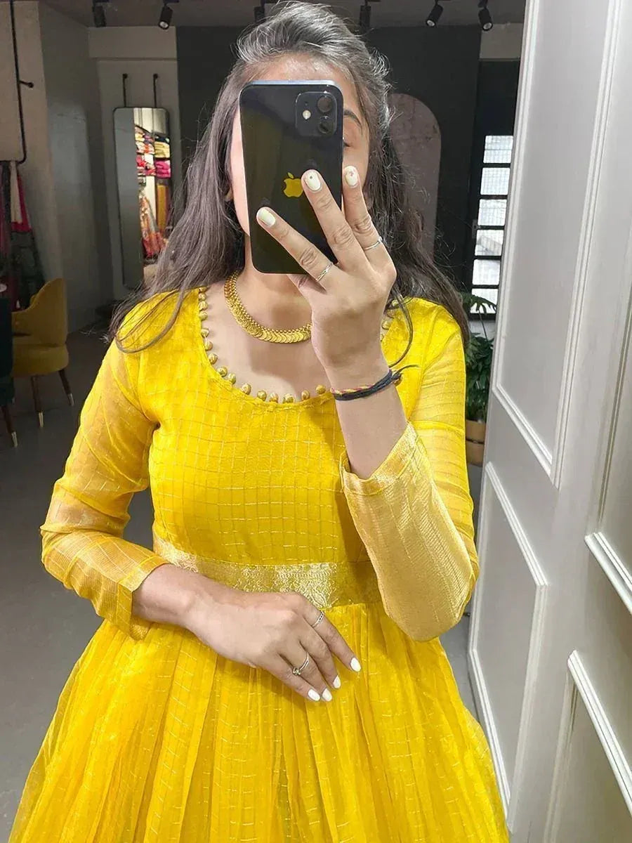 Woman in a bright yellow ethnic gown with gold jewelry, taking a mirror selfie indoors