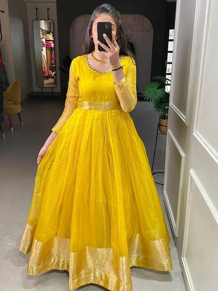 Woman wearing bright yellow ethnic gown with gold border and full sleeves, standing indoors