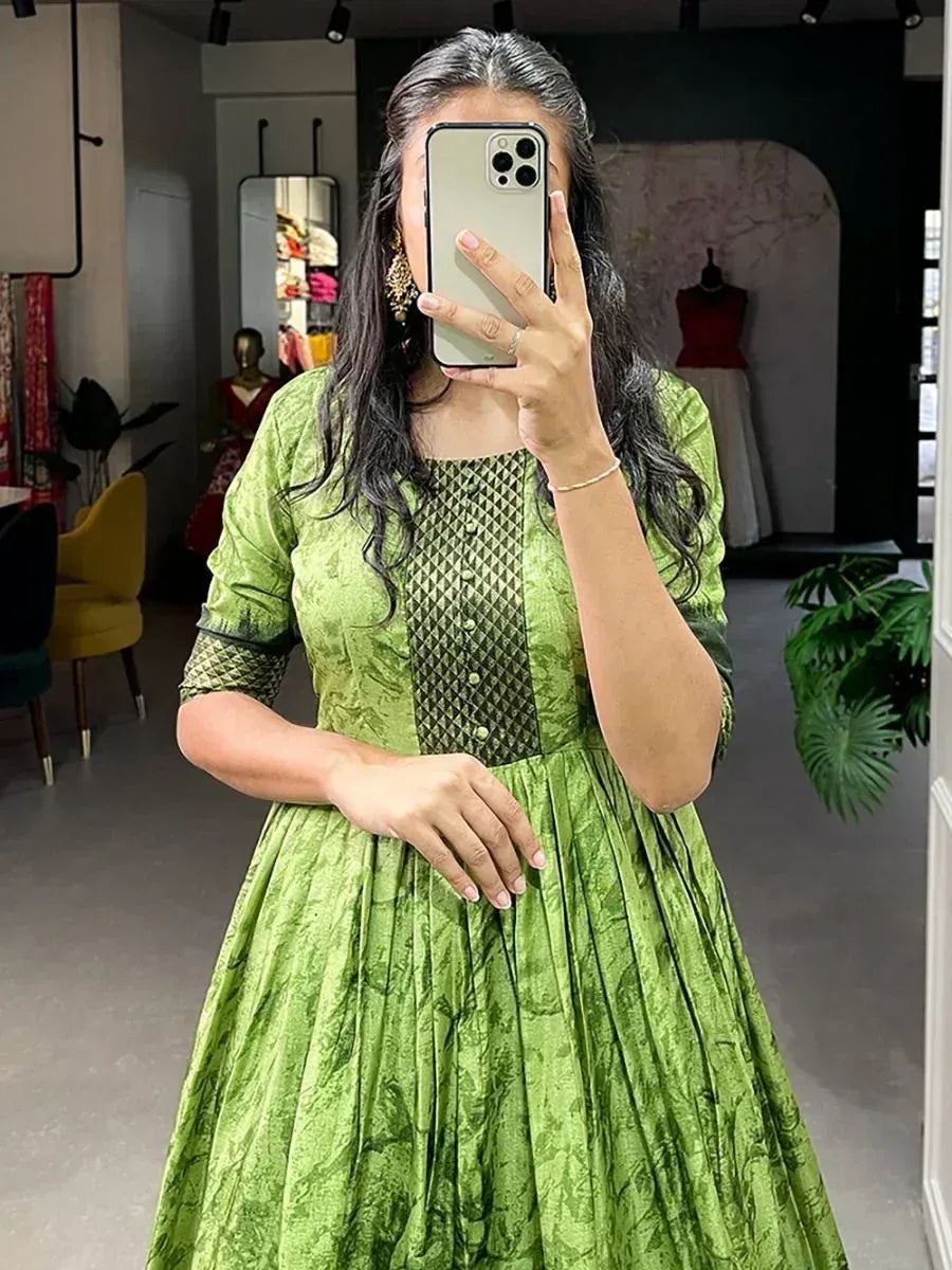 Woman in green ethnic gown with black panel, taking mirror selfie in boutique