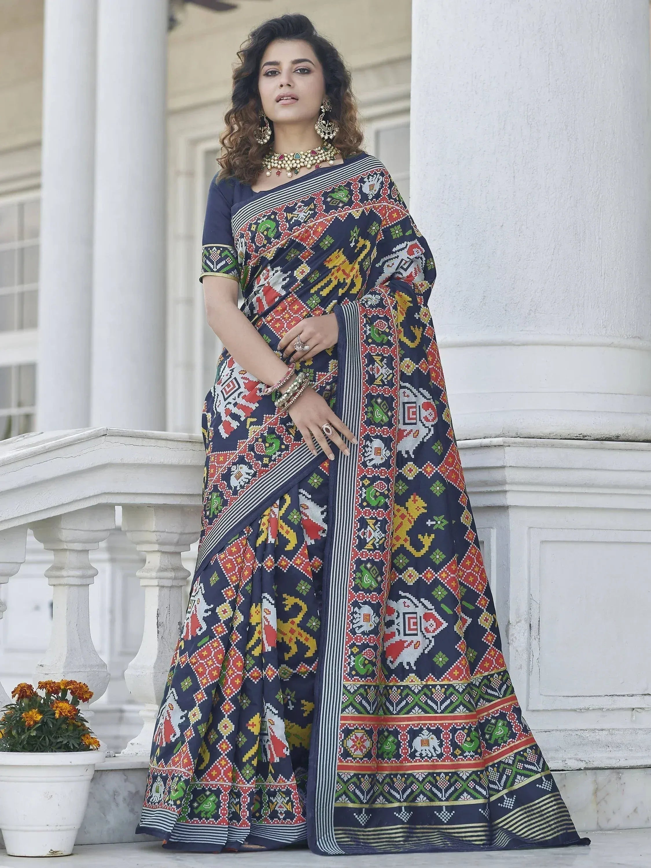 Woman in navy blue printed saree with colorful ethnic motifs, styled with traditional jewelry for festive occasions.