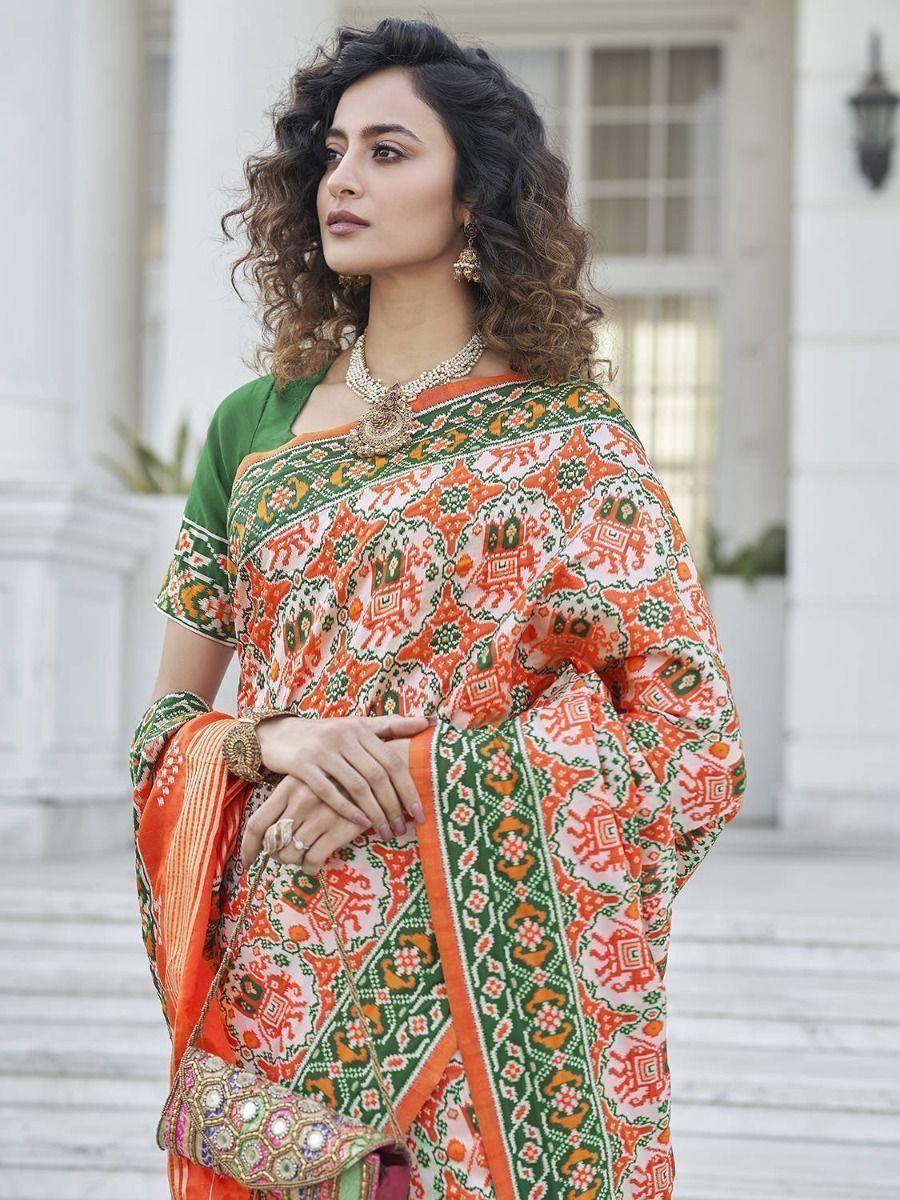 Woman in vibrant orange and green printed saree with ethnic jewelry, perfect for Indian occasions