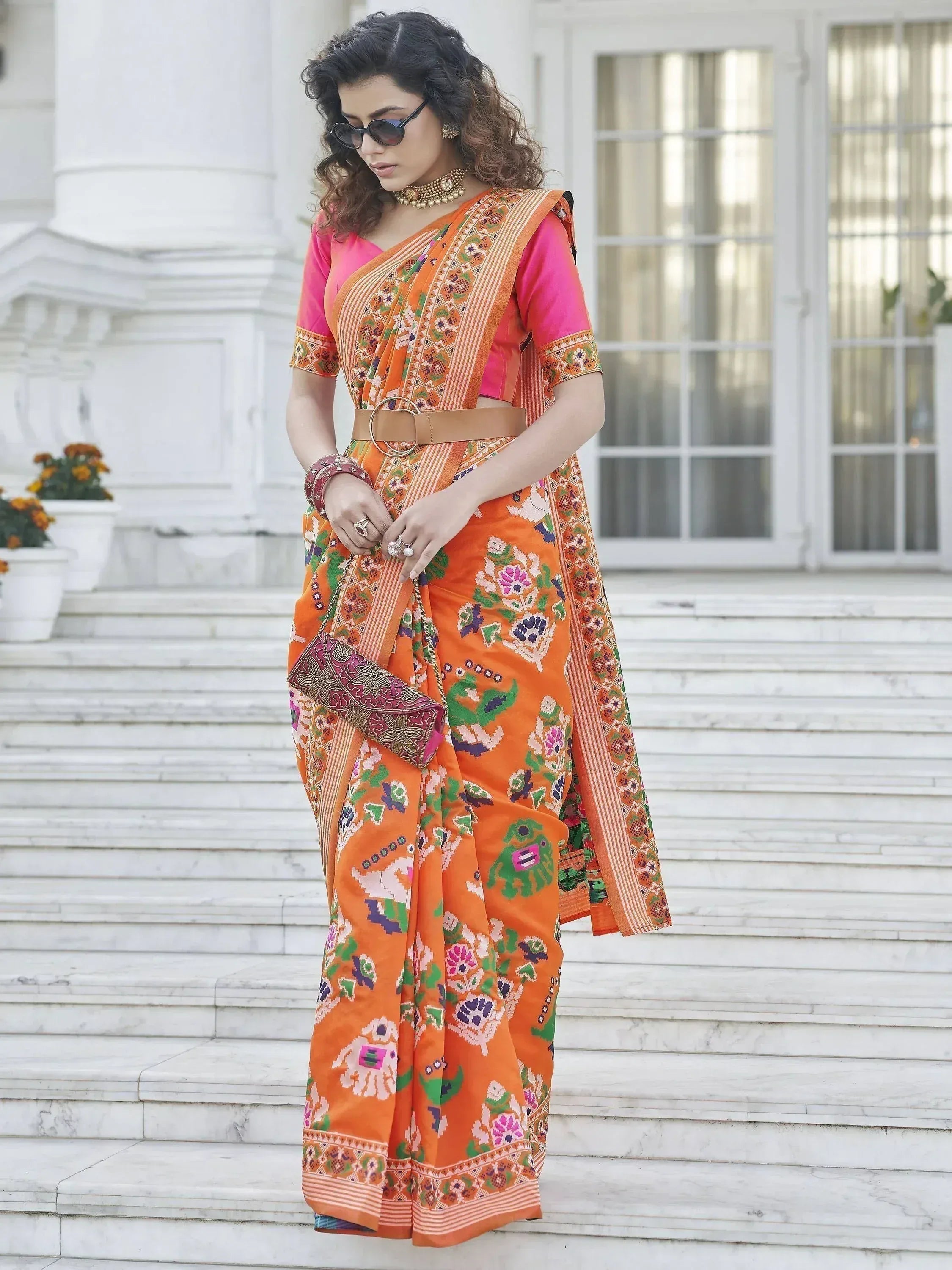 Vibrant orange printed saree with pink blouse, floral motifs, and belt accent, styled for Indian ethnic wear