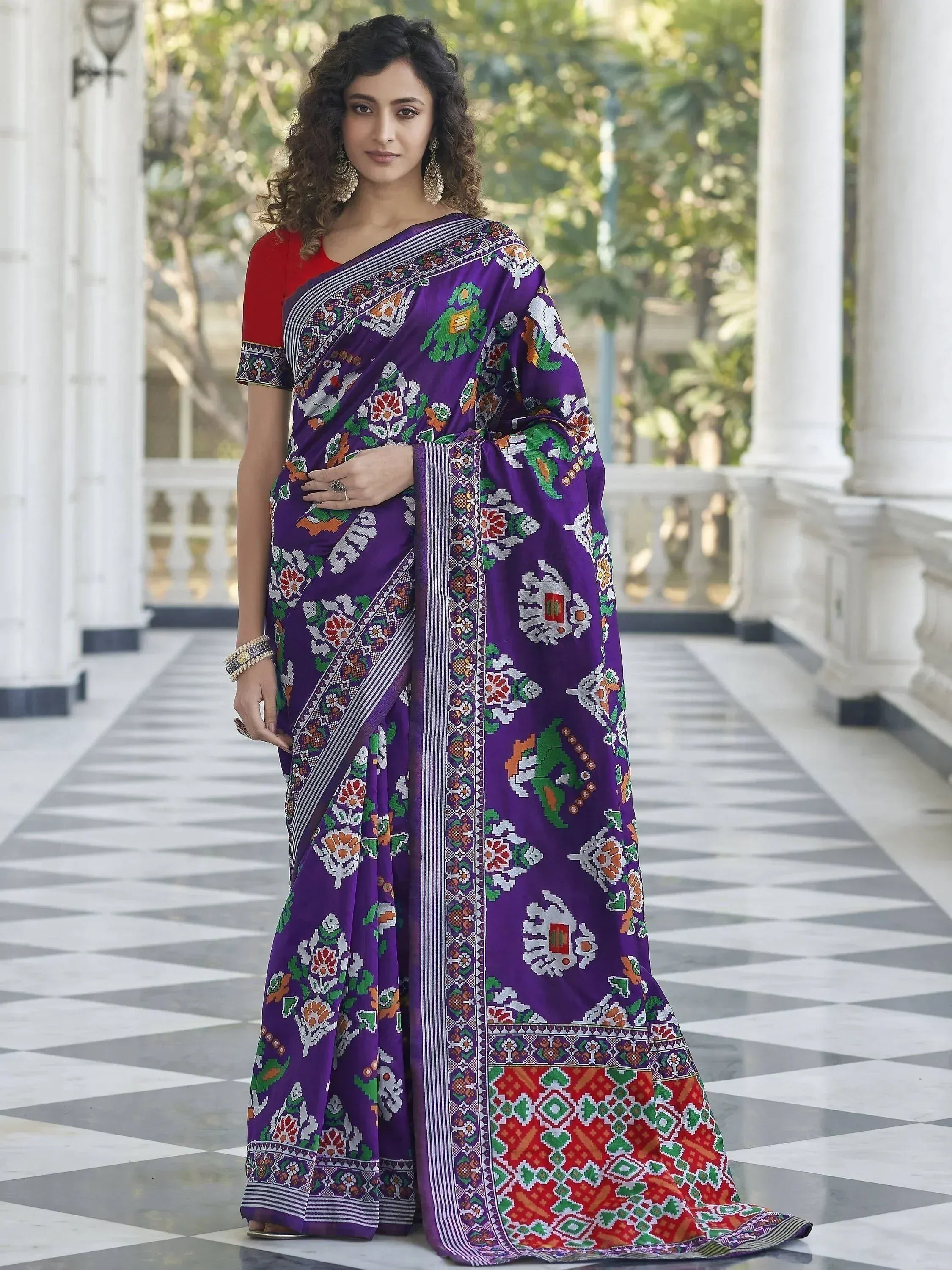 Purple floral saree with vibrant patterns, paired with red blouse, worn by woman in elegant setting