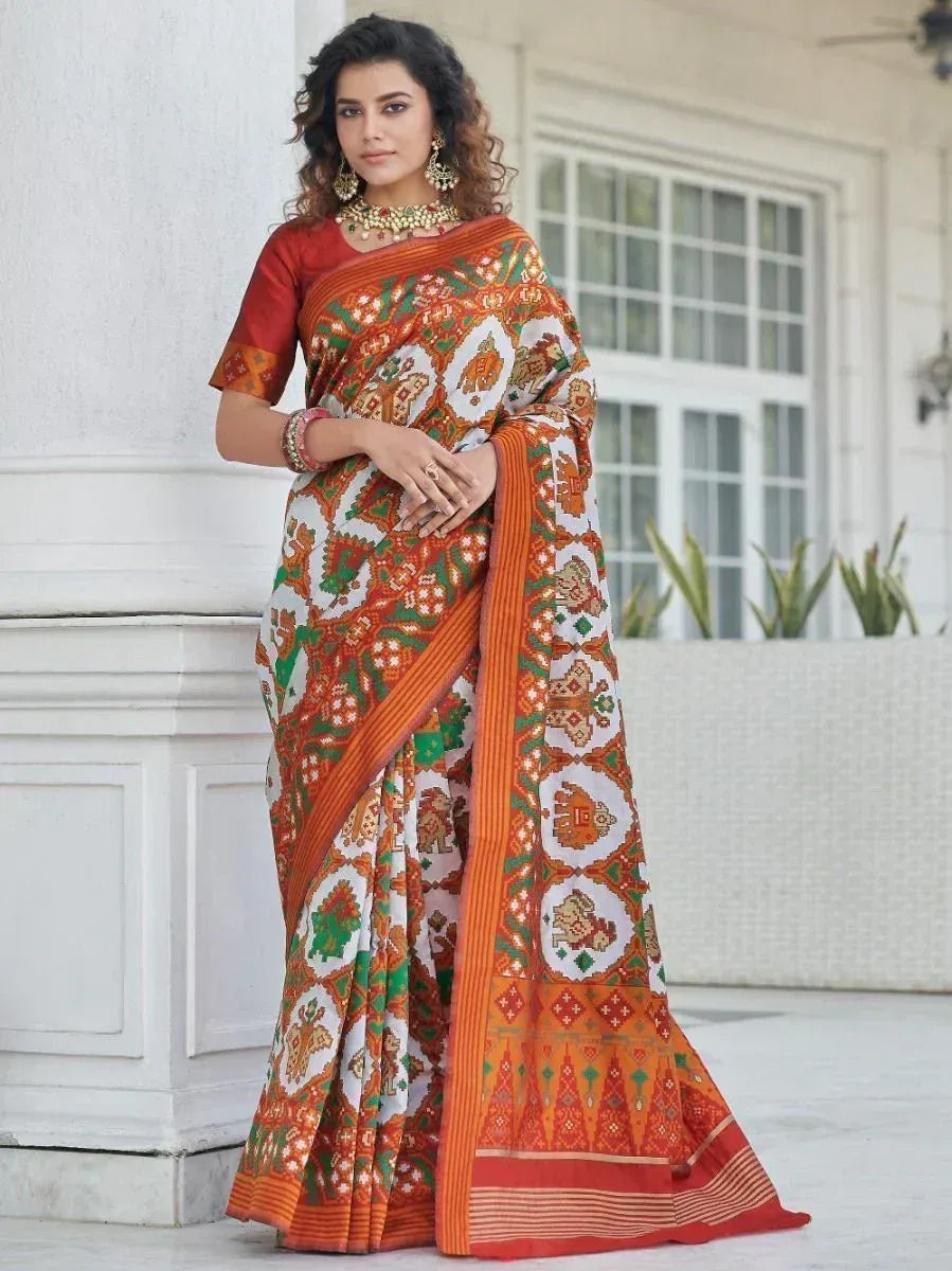 Woman in vibrant orange and green printed saree with traditional Indian motifs, styled with gold jewelry
