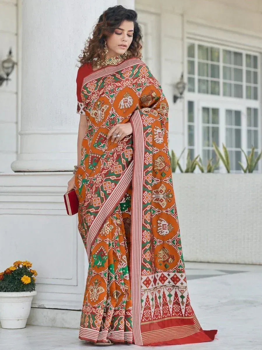 Woman in vibrant orange and green printed saree with elephant motifs, styled with gold jewelry for ethnic occasions