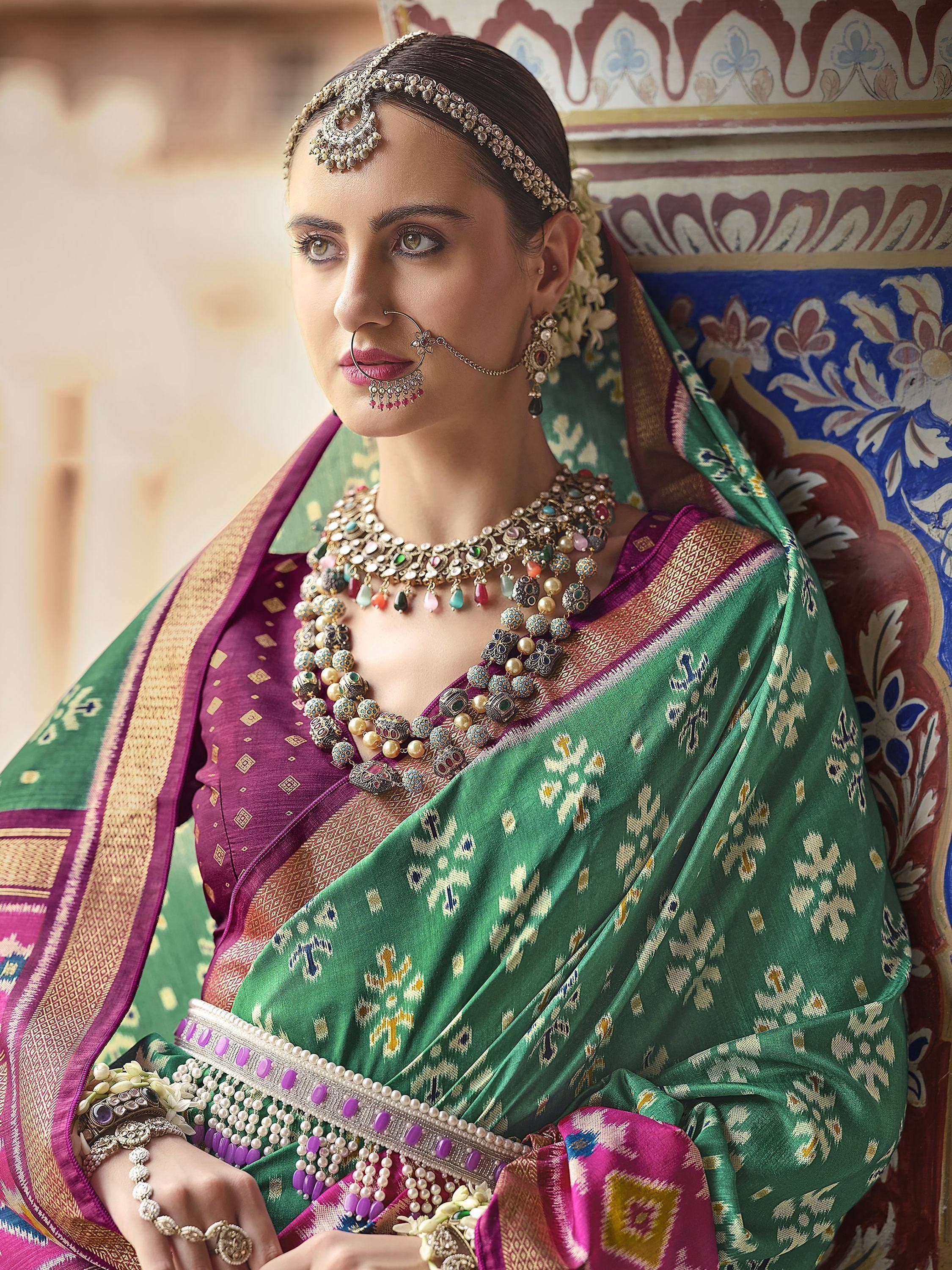 Woman in green and purple ethnic saree with traditional jewelry and floral backdrop